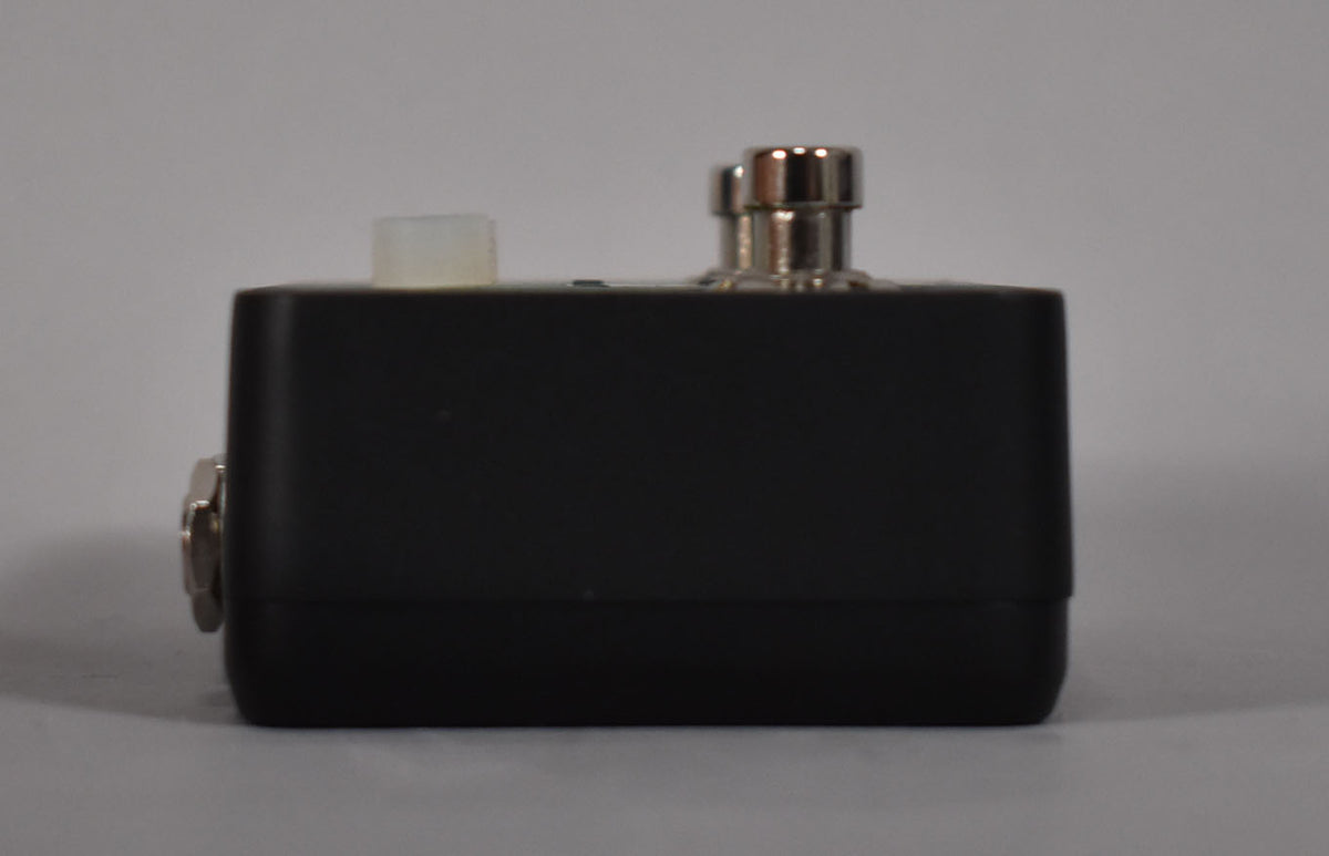 The black pedal is viewed from the right side, showing a silver jack, a translucent white knob, and two silver footswitches.