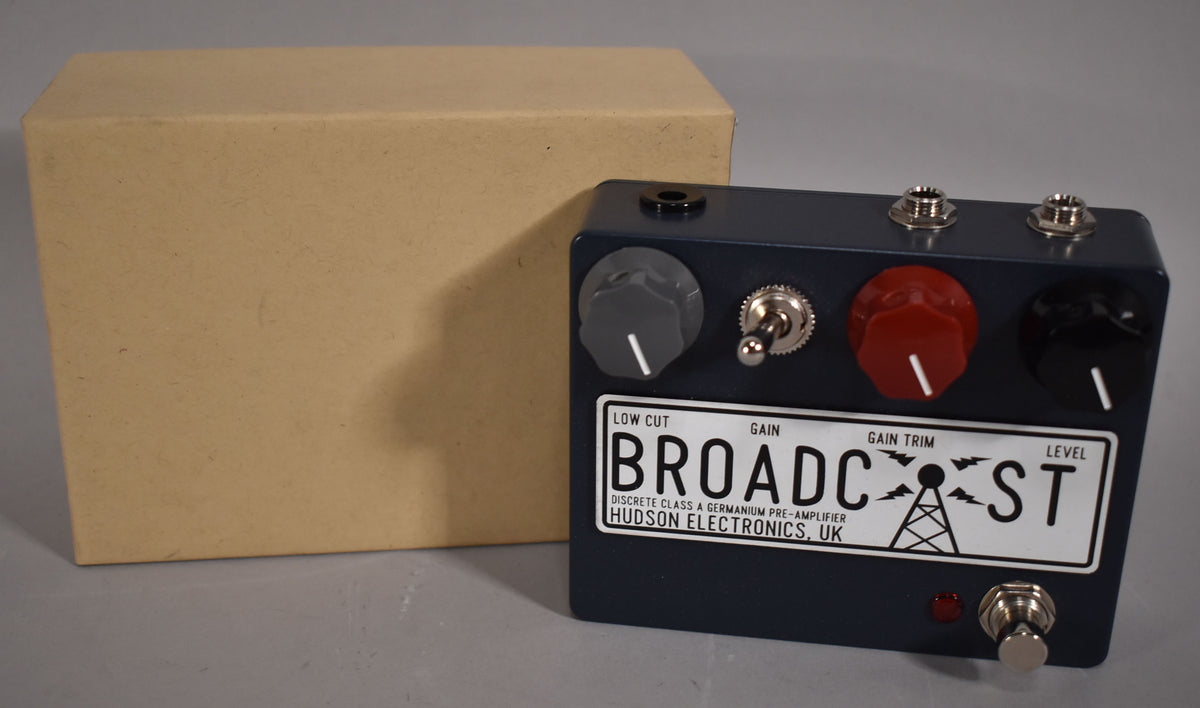 A dark blue guitar pedal with a white license plate-style label, three knobs (grey, red, black), two toggle switches, and a footswitch.