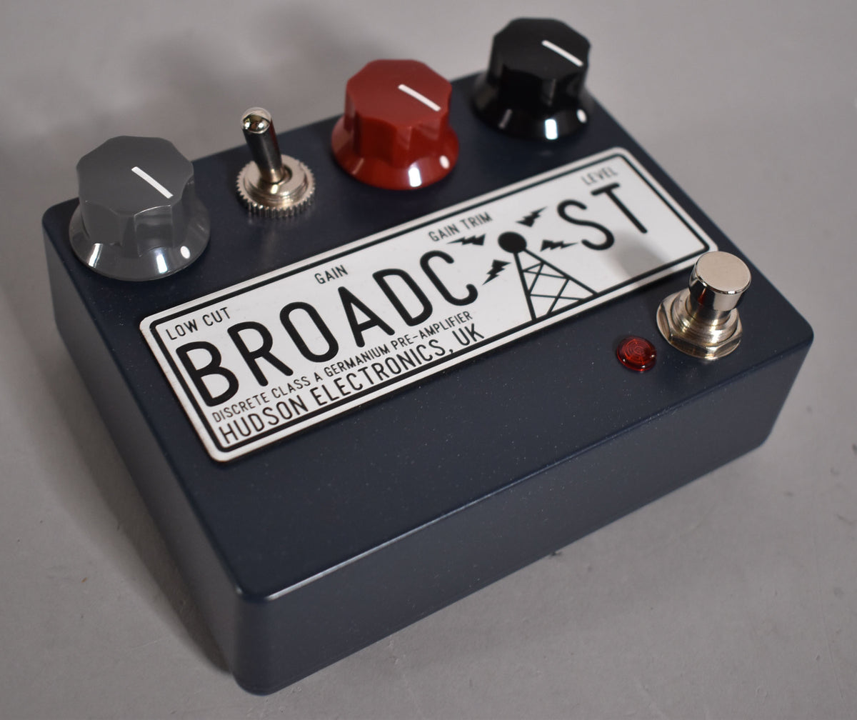 A dark grey pedal with a white label, three knobs (grey, red, black), a toggle switch, a footswitch, and a red indicator light.