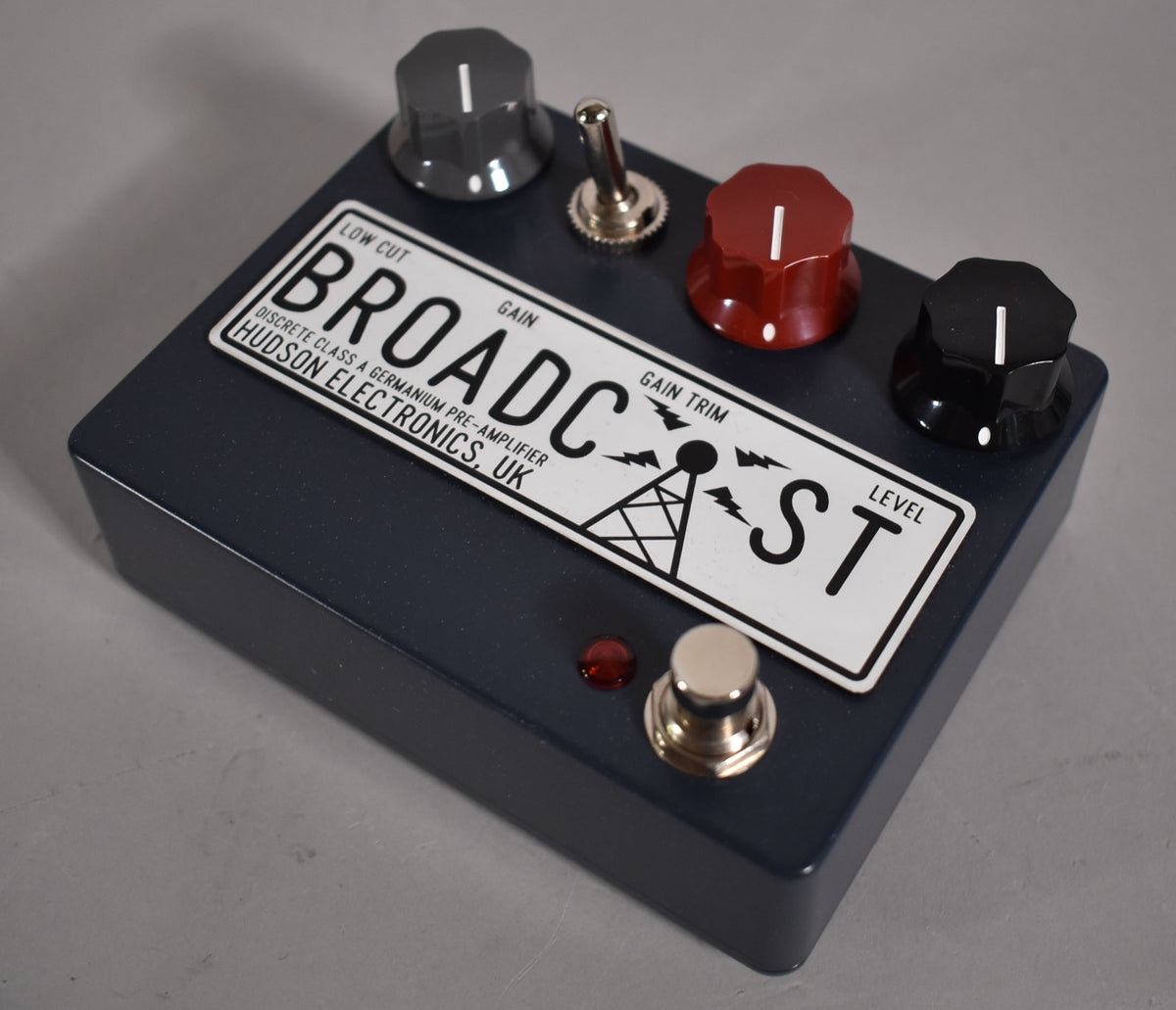 A dark gray pedal with a white label, three control knobs (gray, red, black), a toggle switch, and a footswitch.