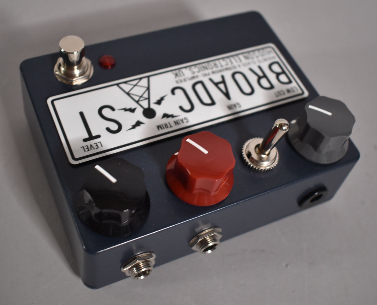 A dark blue pedal with a white label, three large knobs (black, red, grey), a toggle switch, a footswitch, and two input jacks.