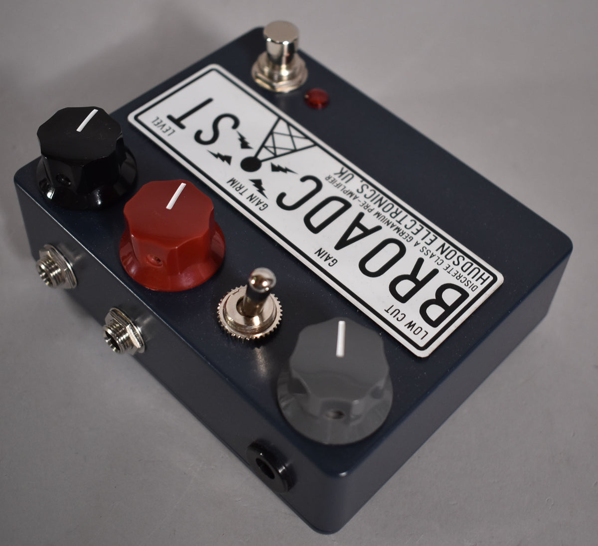 Dark blue pedal with a white label, three large control knobs (black, red, grey), a chrome footswitch, a red LED, and a chrome toggle switch.