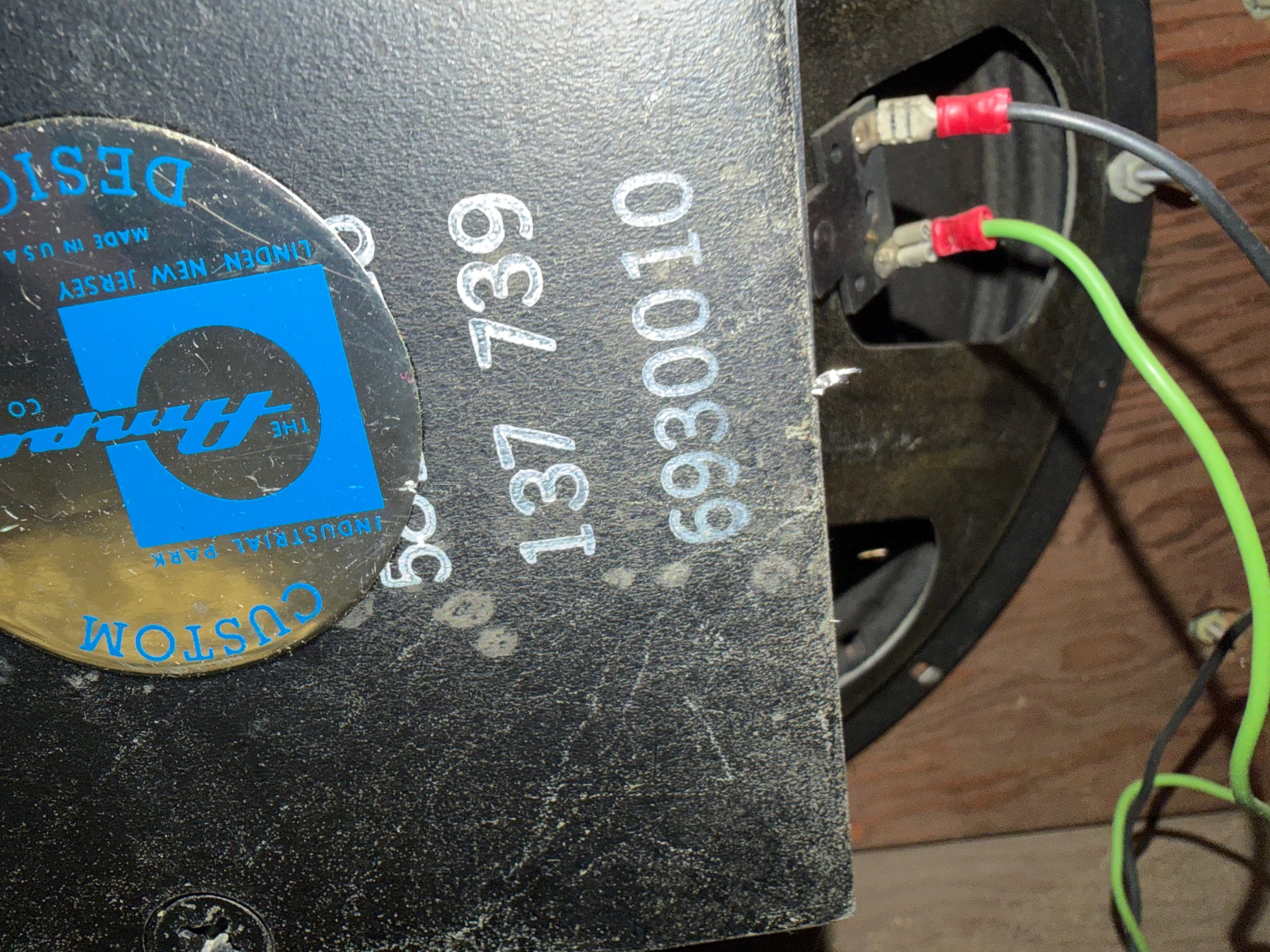 Close-up of the speaker's rear, showing the black cabinet with white stenciled numbers, a round blue and silver sticker, and red and green wires.