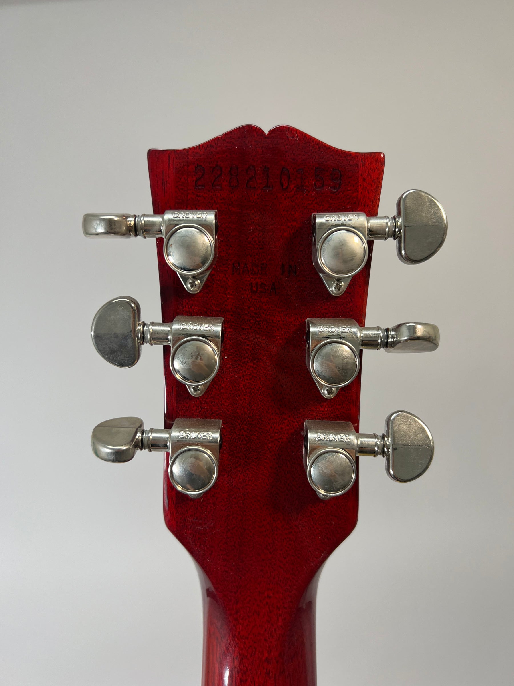 The back of a deep red guitar headstock with six Grover tuners and a serial number stamped at the top.