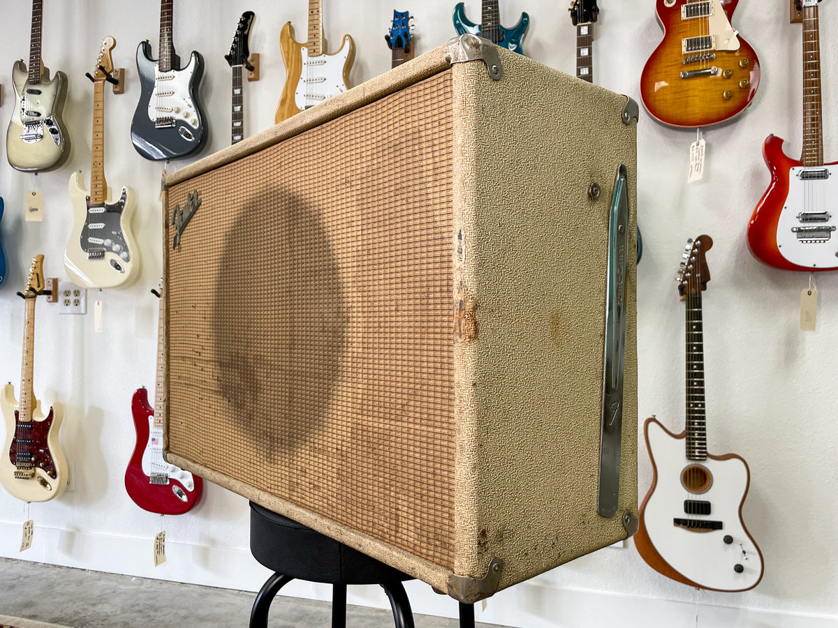 Front-left view of a blonde speaker cab with a heavily stained grille cloth, worn corners, and a chrome side handle.
