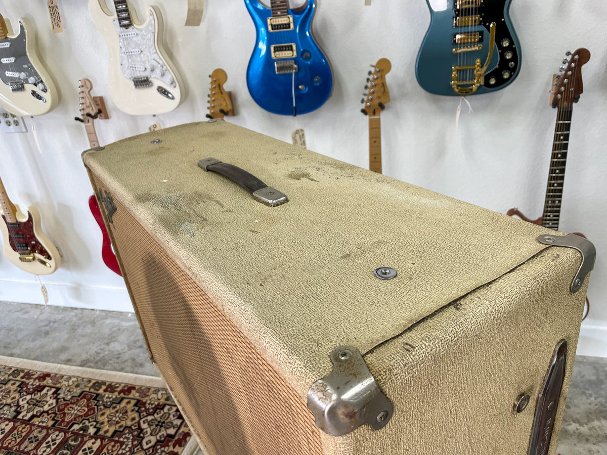 Angled view of the blonde speaker cab, showing its textured finish, brown handle, metal corner protectors, and some visible wear.
