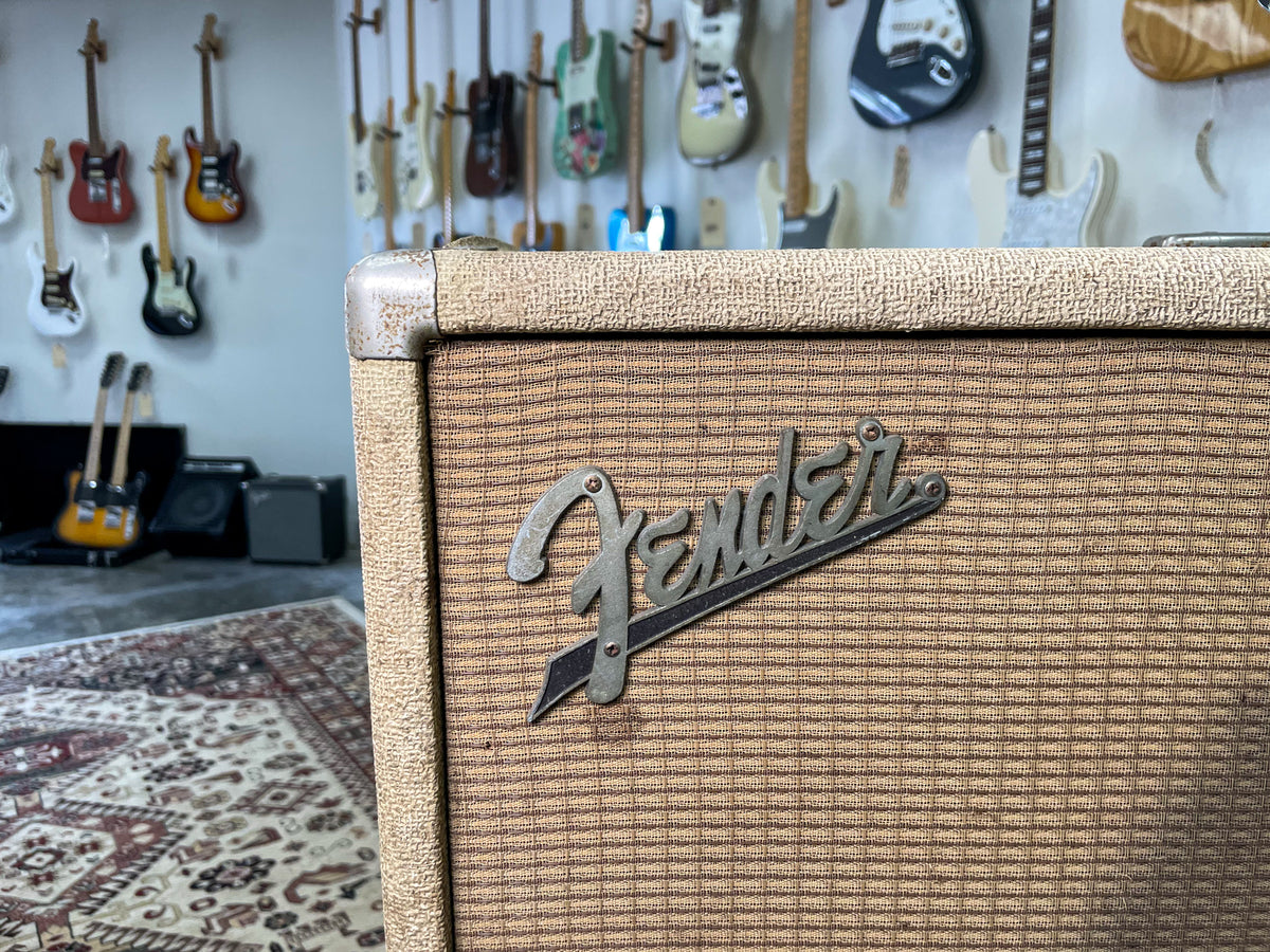 Close-up of the speaker cab's upper right, showing blonde tolex, brown grille cloth, and a tarnished silver logo.
