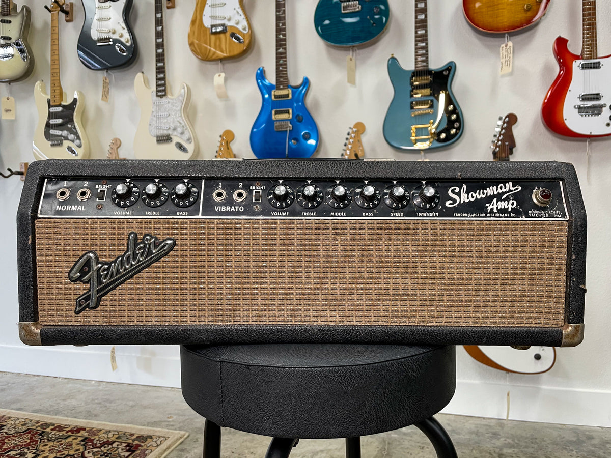Front view of a black amp head with a brown grille, silver control panel, and 12 black knobs, showing corner wear.