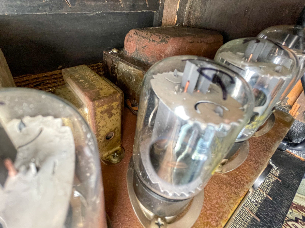 Close-up of the amp's top, showing three large glass vacuum tubes and two rusty, rectangular transformers on a worn metal chassis.