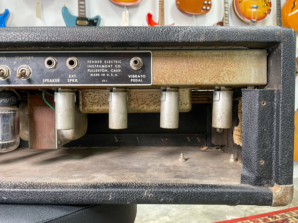 Rear view of the amp head, showing the black tolex covering, rusty metal chassis, four tube sockets, and speaker/pedal jacks.
