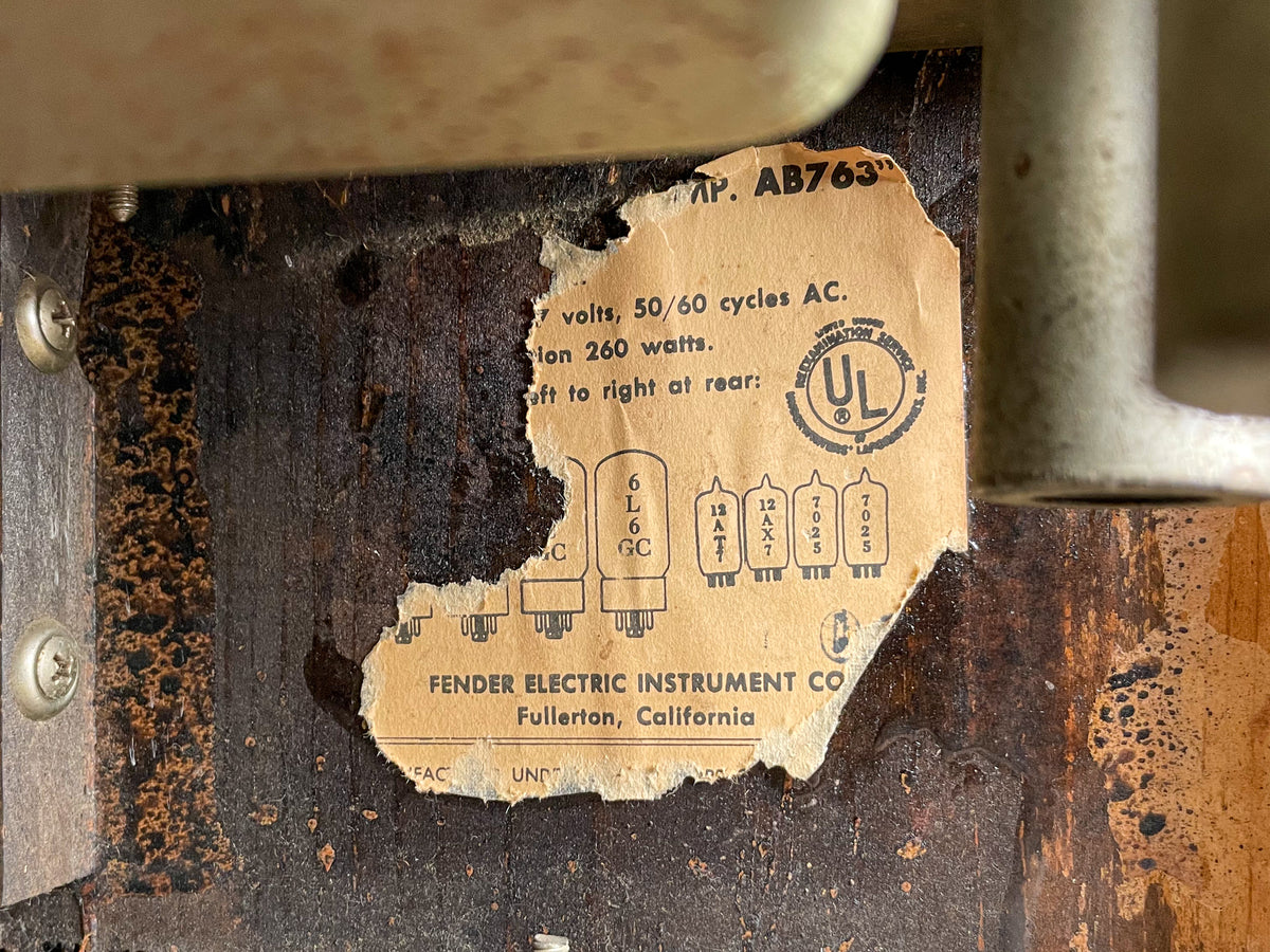 Close-up of the amp's interior, showing a torn, yellowed paper label with tube diagrams and text, affixed to dark, worn wood.