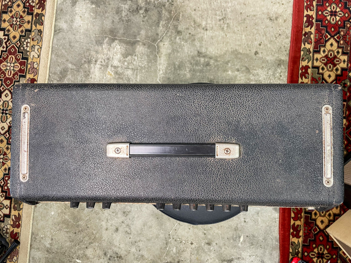 Top-down view of the black tolex amp head, showing a worn handle, metal corner protectors, and a row of knobs along the front edge.