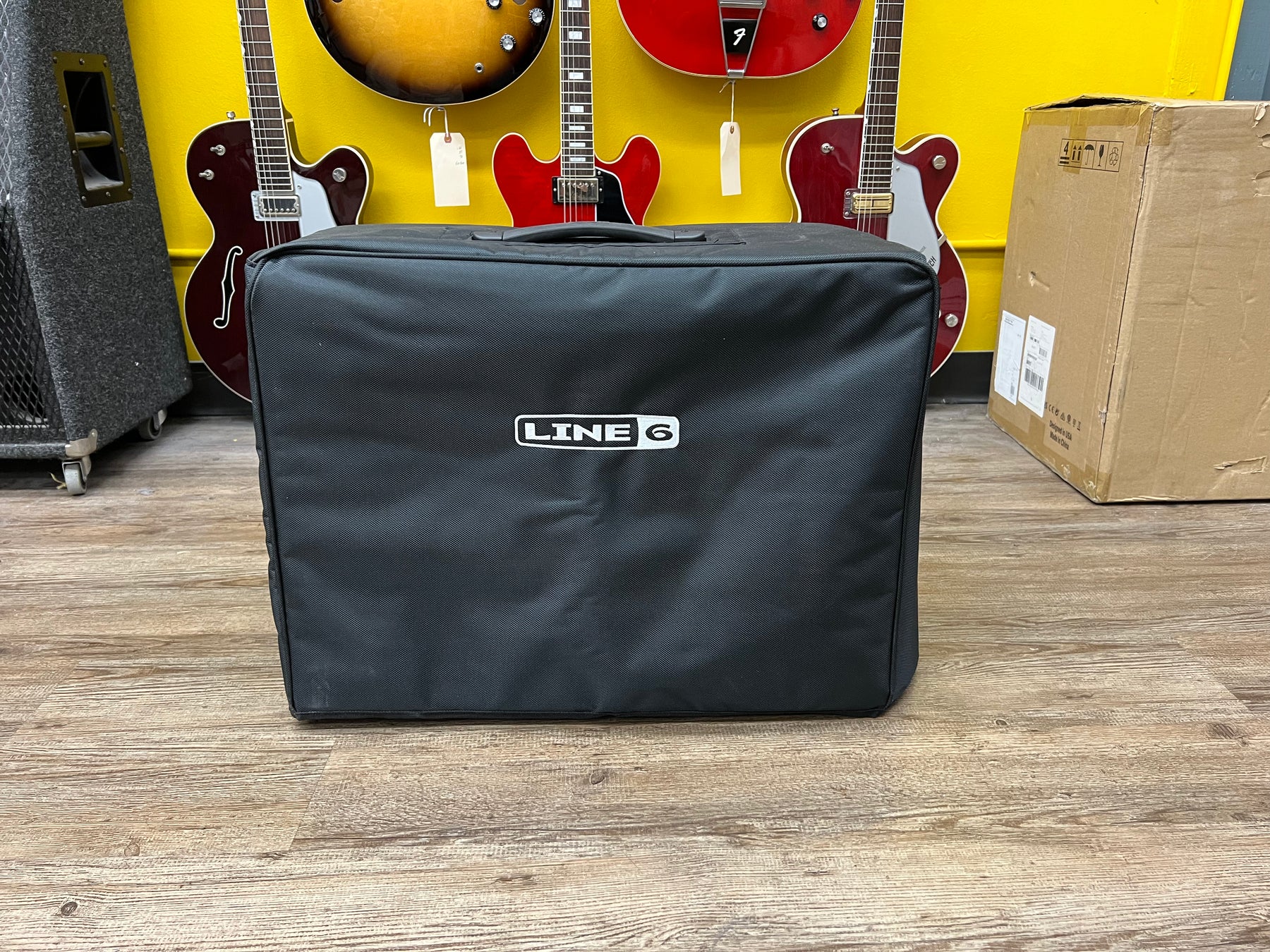 The black soft cover for the amp is shown from the front, with a white logo and a top handle visible.