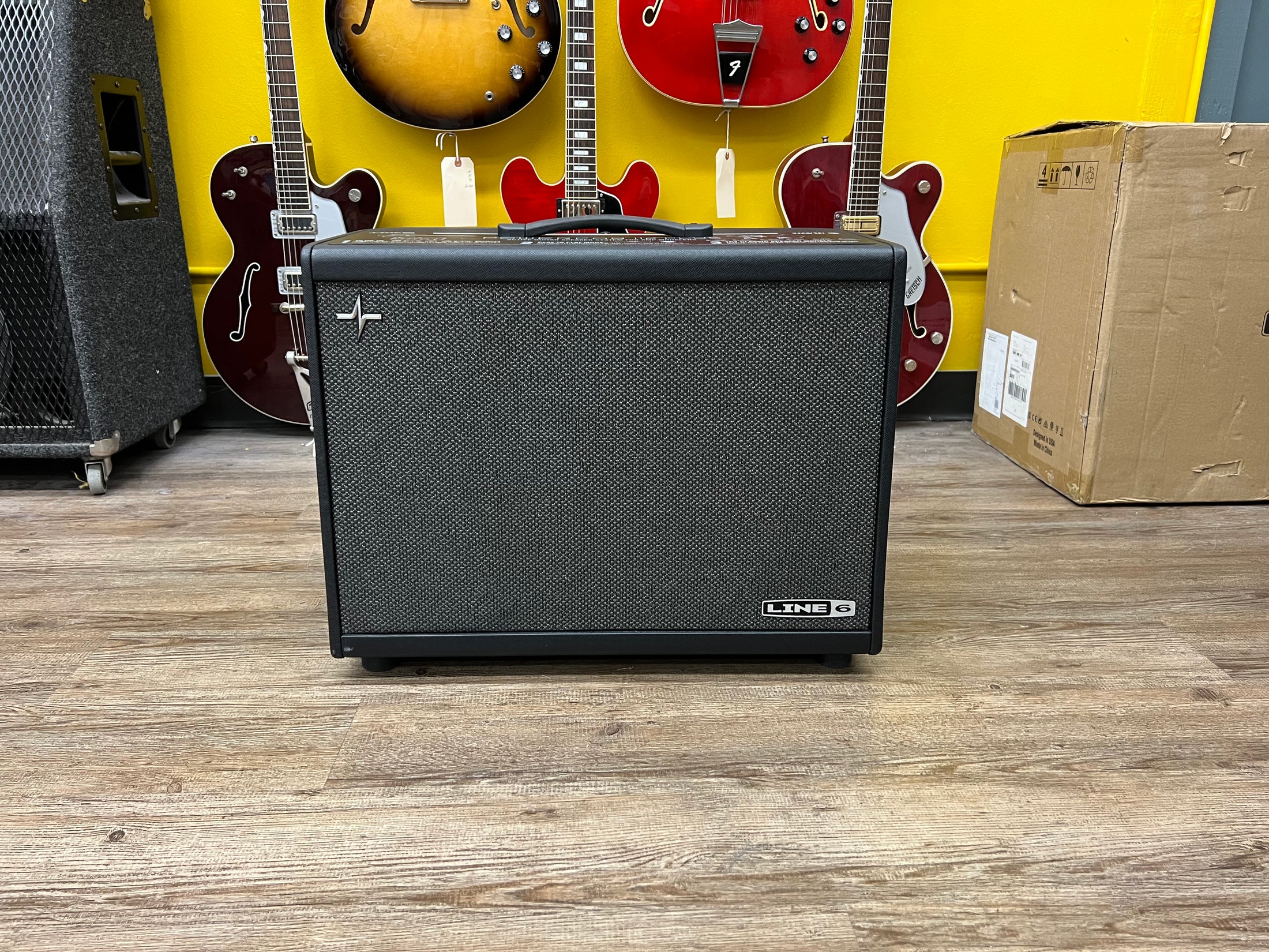A black guitar amp with a dark gray speaker grille, viewed head-on, showing a silver cross-shaped emblem on the upper left.