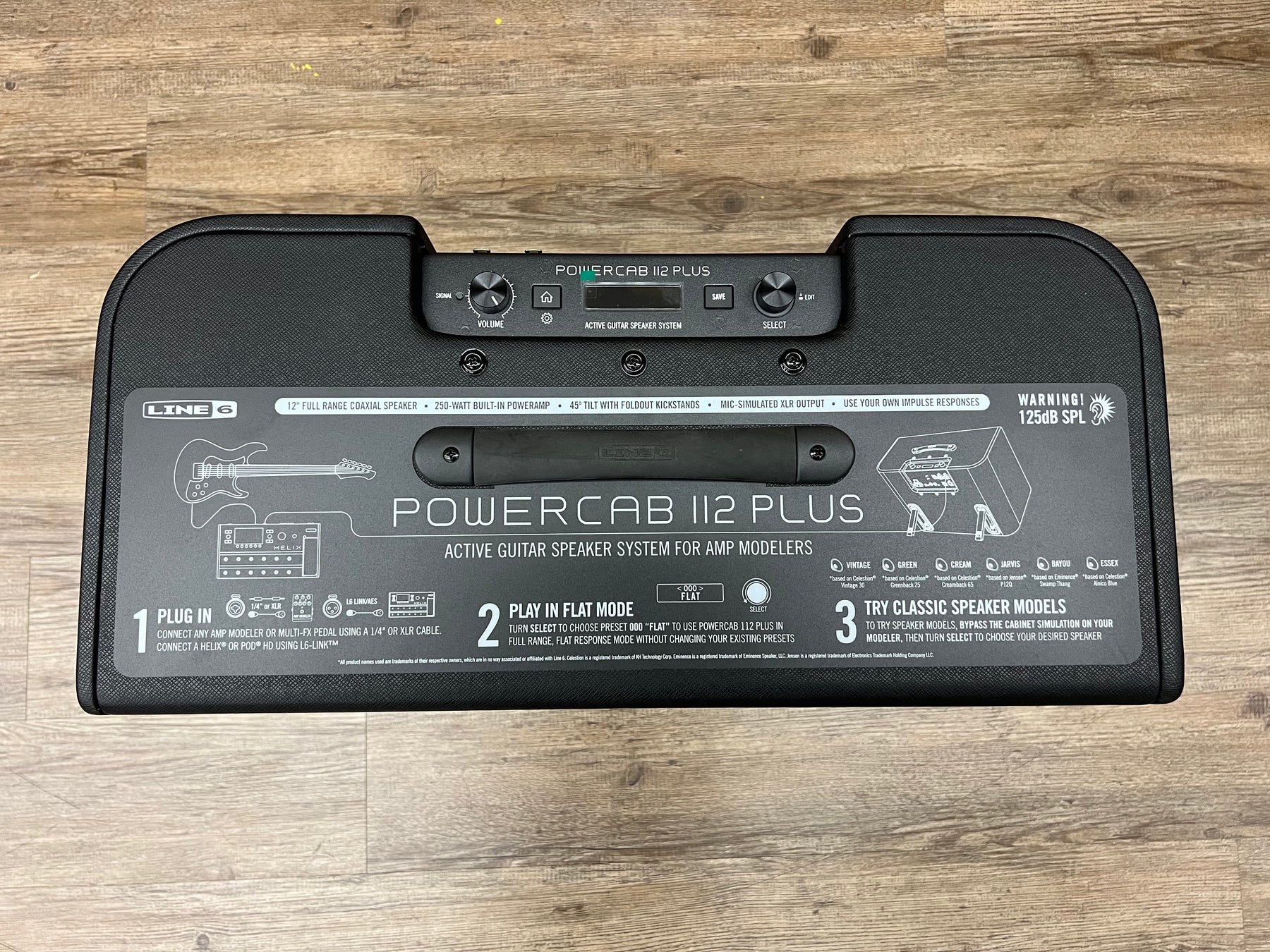 The black amp is seen from above, showing the top control panel and a large instruction sticker on the front.