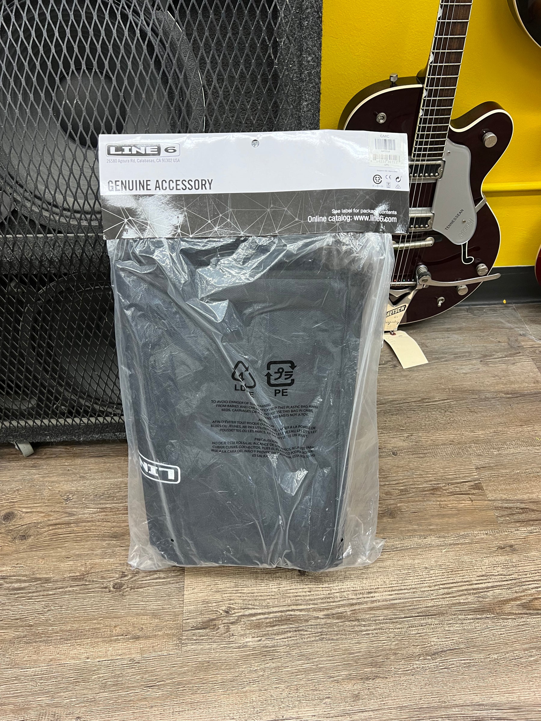 A black padded amp cover, still sealed in its clear plastic bag with a white and black "Genuine Accessory" header card.