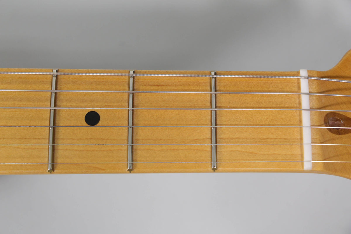 Close-up of the light maple fretboard, showing the first five frets, a black dot inlay on the third fret, and a white nut.