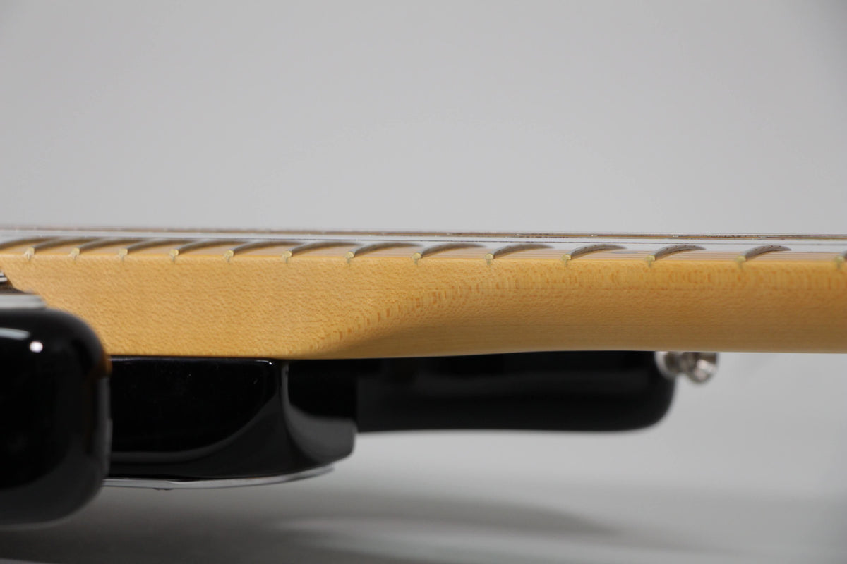 Close-up of the guitar's maple neck and fretboard, showing the frets and the smooth transition to the black body.