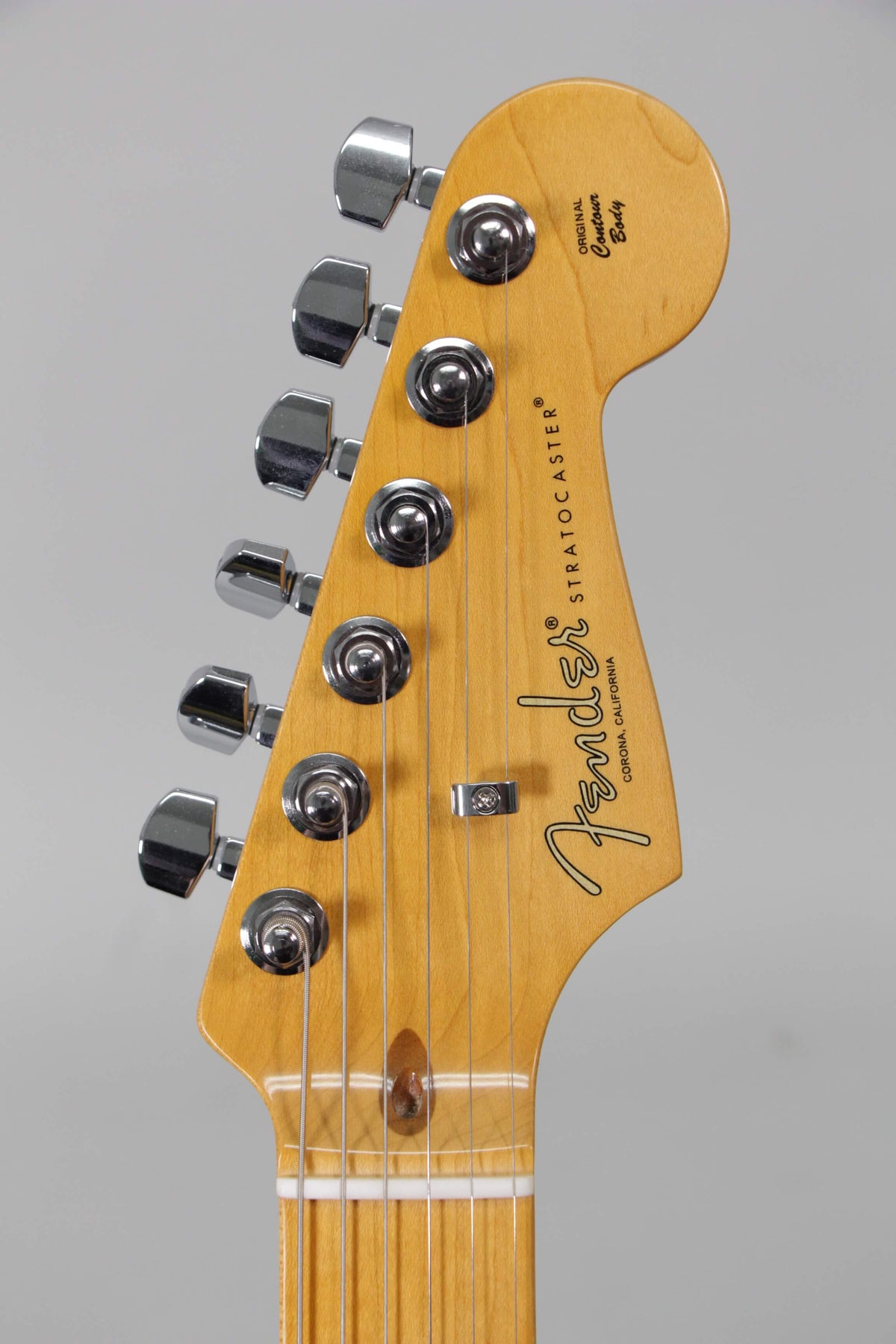 Close-up of the guitar's headstock, angled slightly left, showing six chrome tuners, a string tree, and a light maple finish.