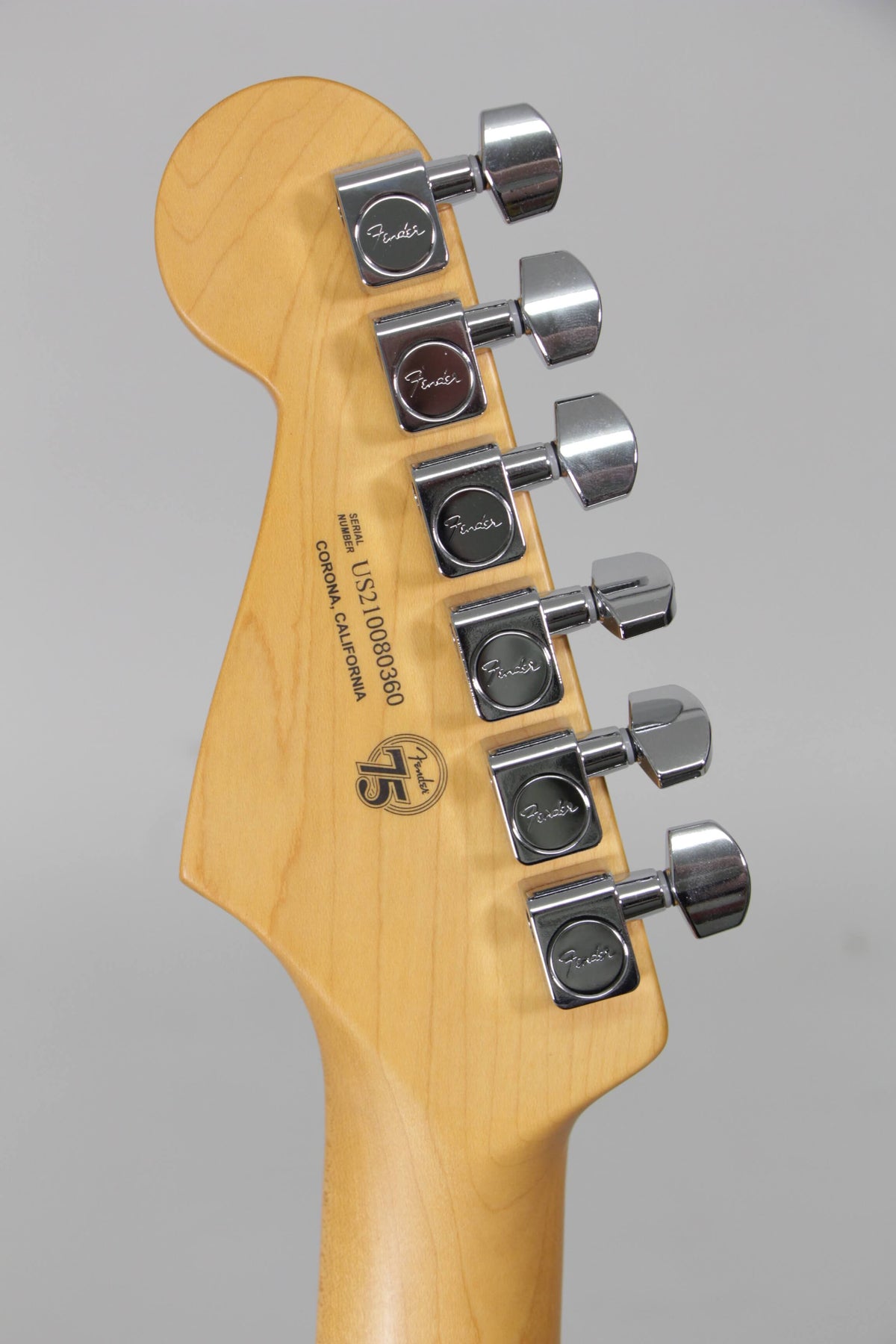 The back of a light maple headstock with six chrome tuners and a "75" anniversary logo.