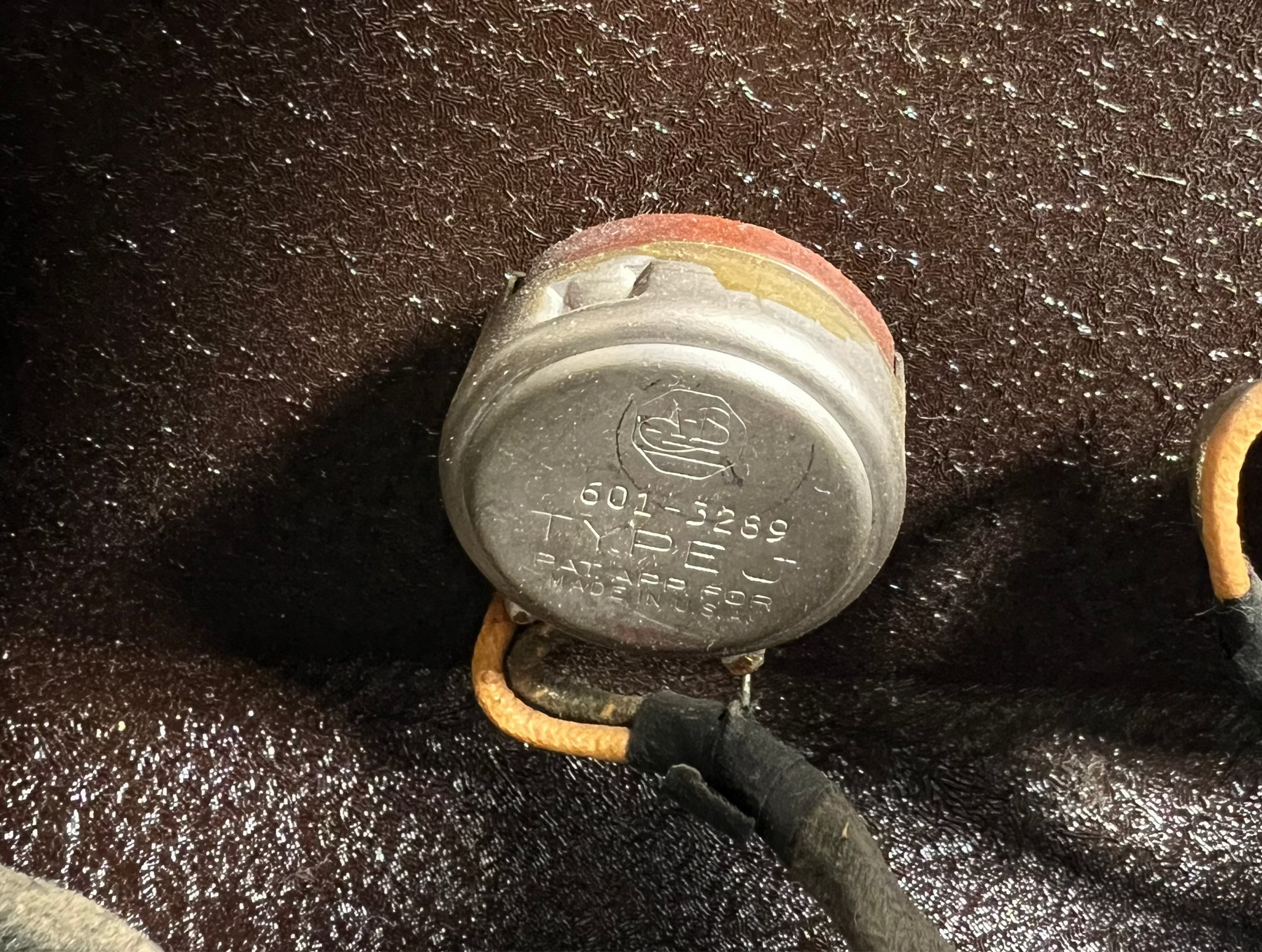 Close-up of a silver metal potentiometer with a red top, showing connected wires and some wear, against a dark textured background.