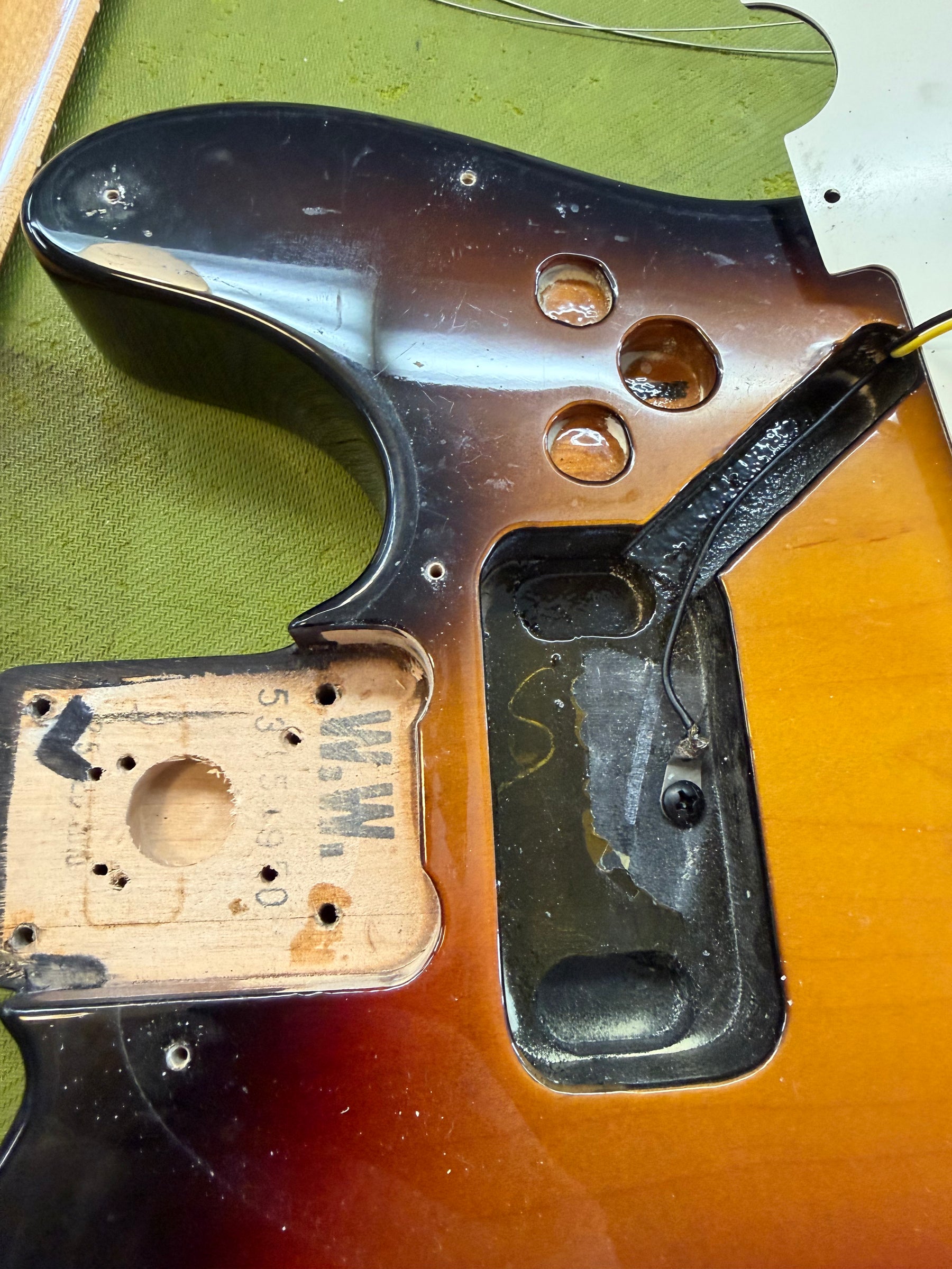 Overhead view of a sunburst guitar body, showing the neck pocket, control cavity, and pickup routes, with visible wear.