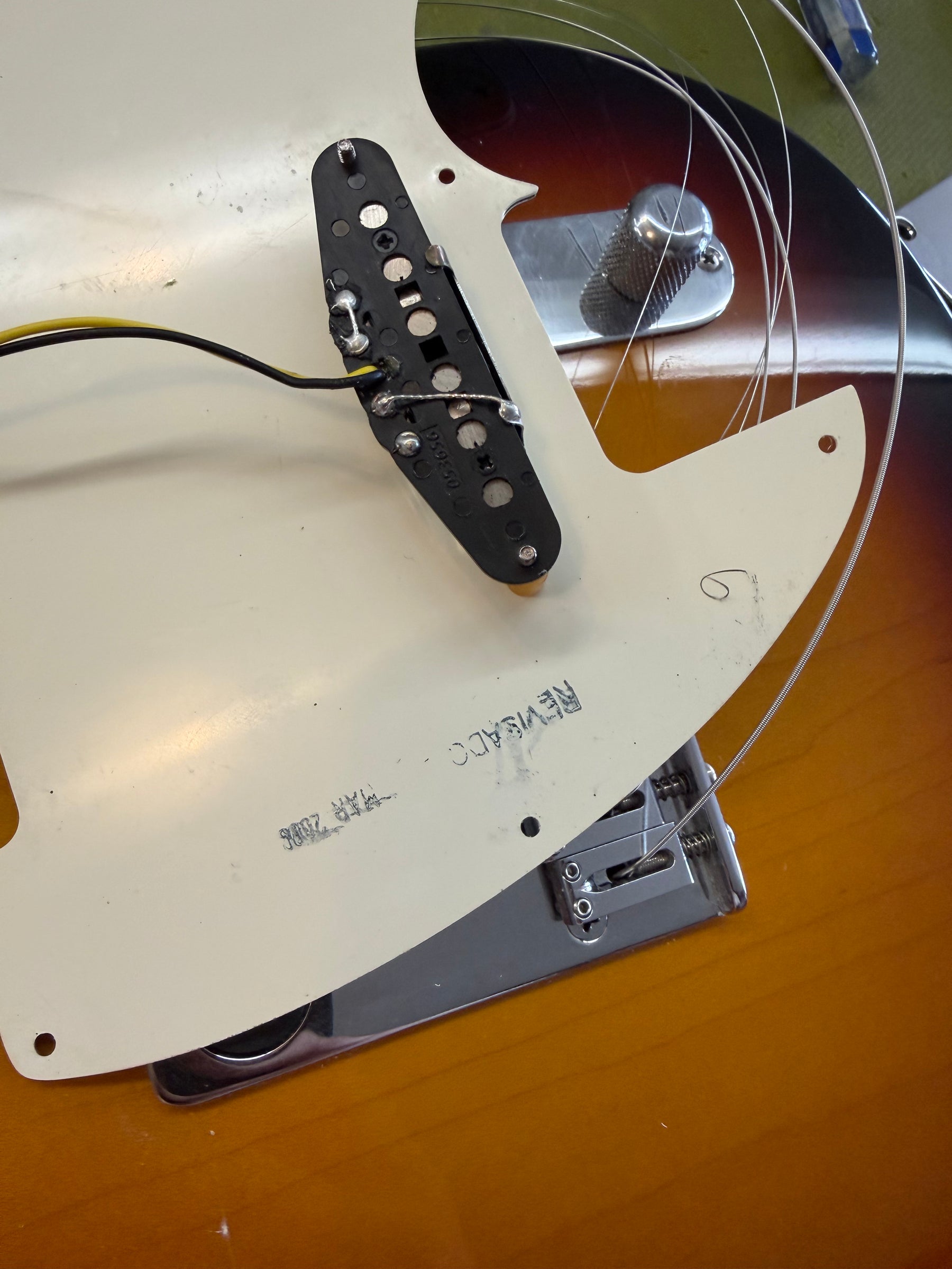 Close-up of the guitar's sunburst body with the white pickguard partially lifted, revealing a black single-coil pickup and wiring.