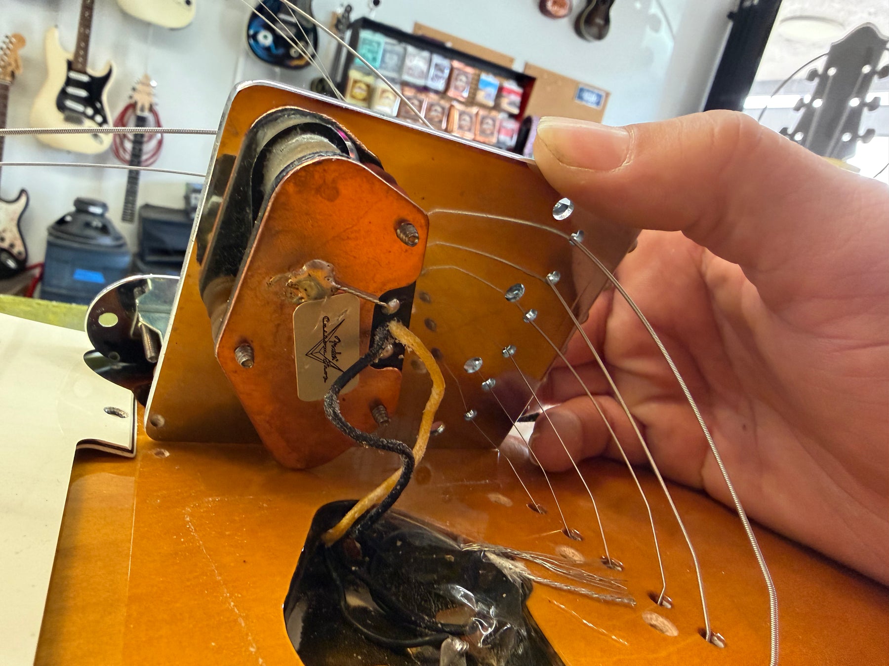 Close-up of the guitar's sunburst body, showing the bridge pickup's wiring and a hand holding the chrome bridge plate.