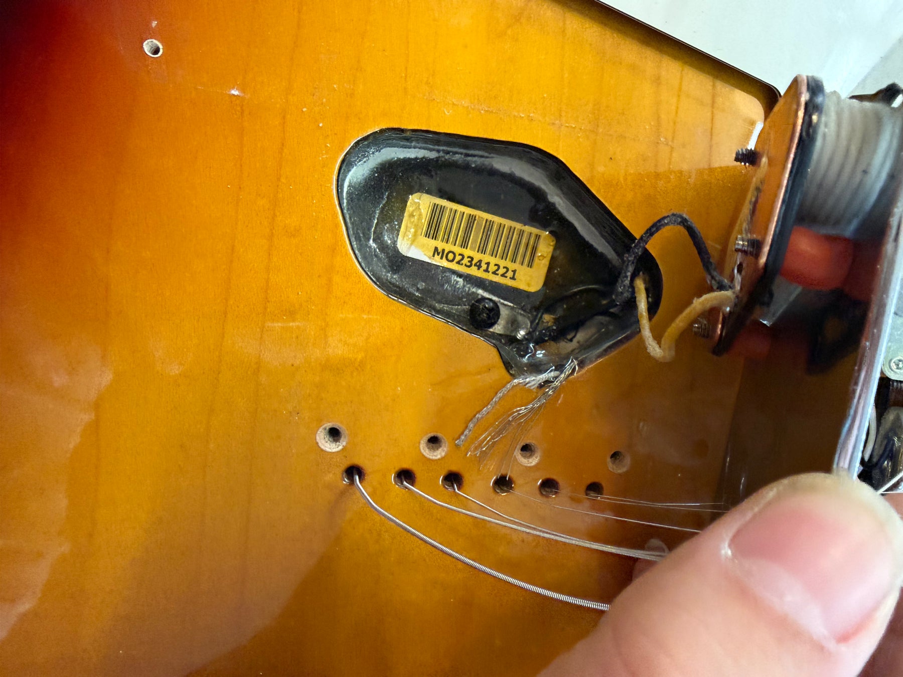 Close-up of the sunburst body cavity, showing a black pickup with a yellow barcode sticker, wiring, and string-through holes.