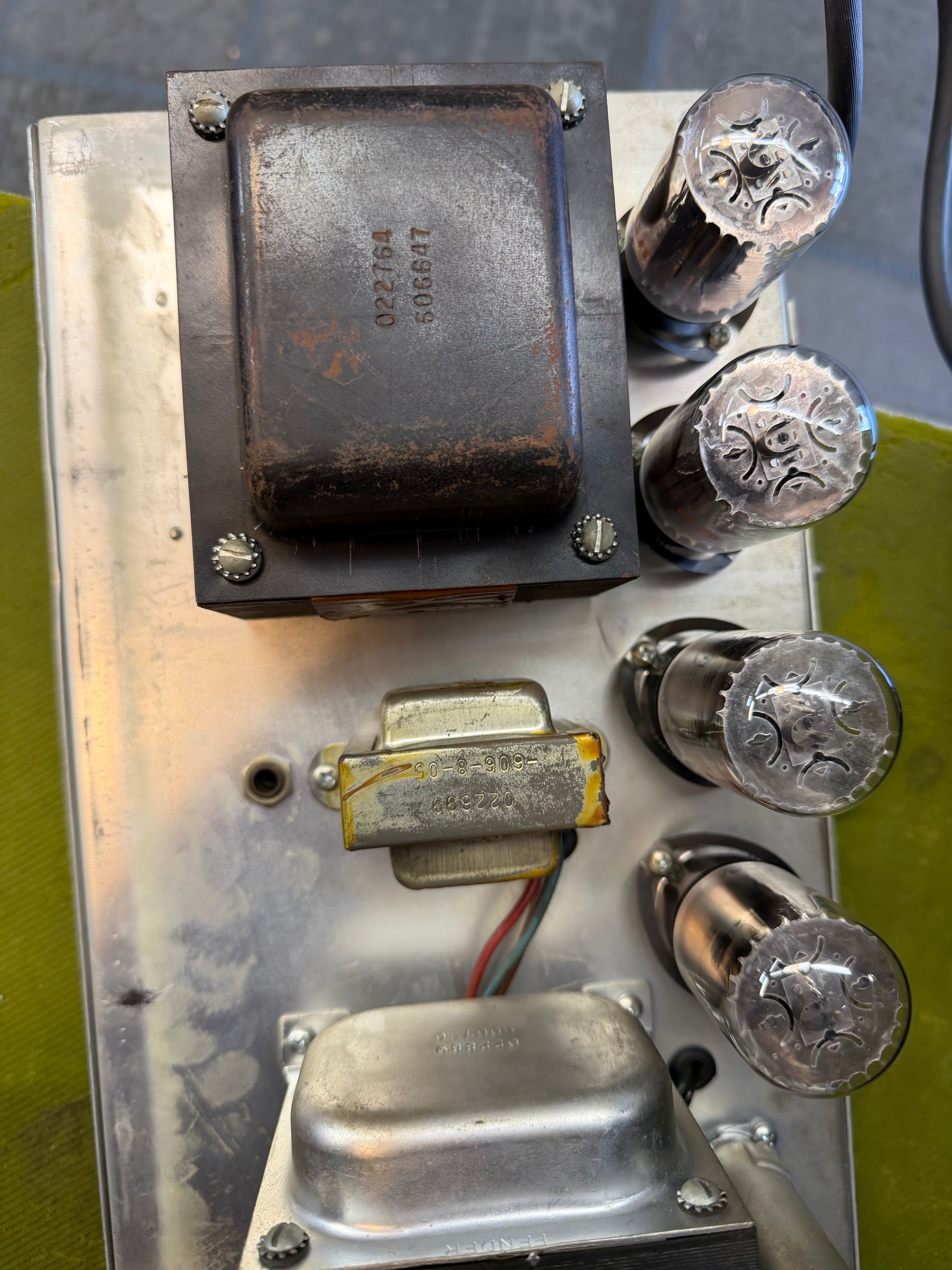 Overhead view of the amp's internal chassis, showing four large vacuum tubes, two transformers, and a silver metal plate with wear.