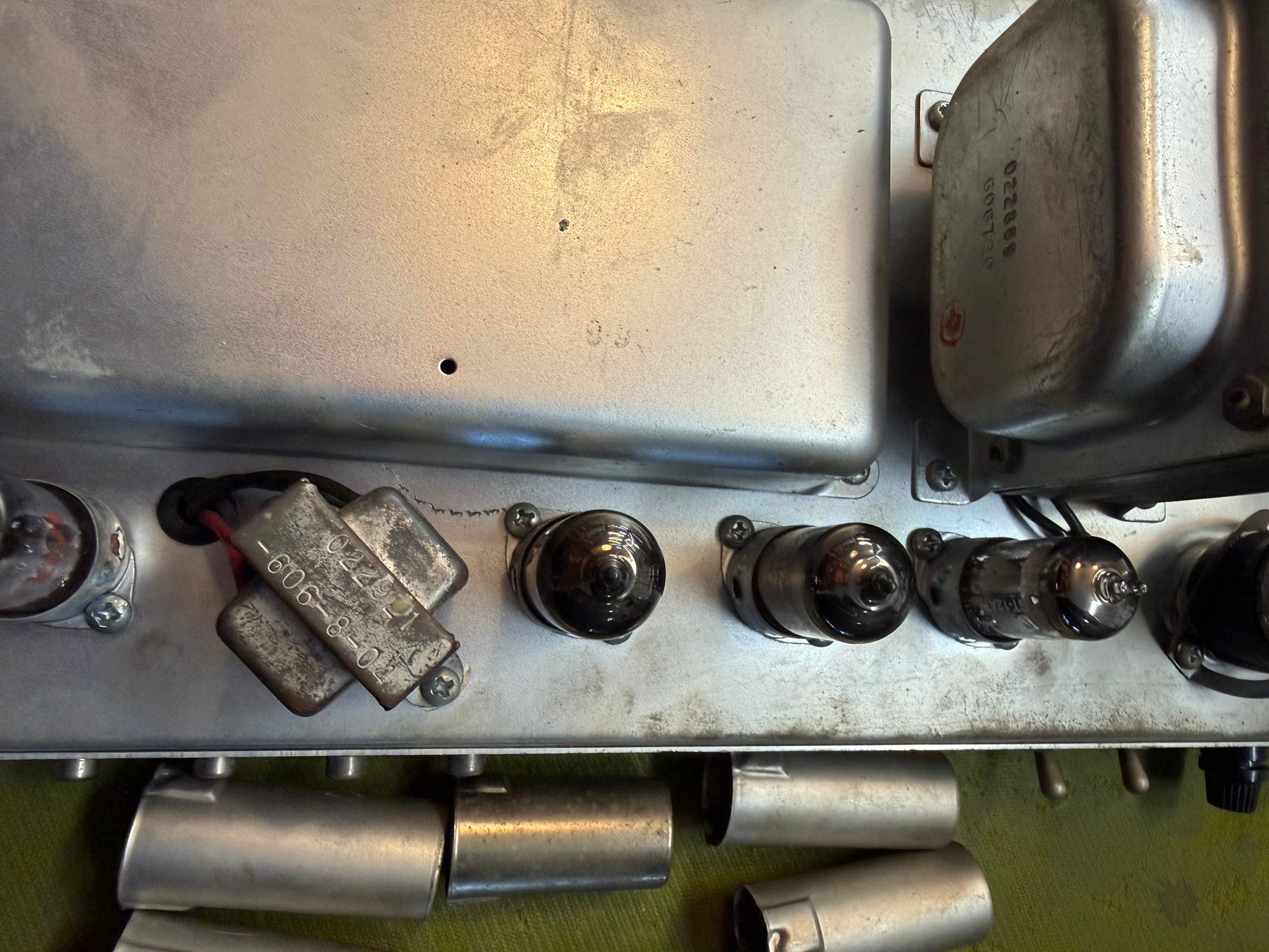 Overhead view of the amp's silver chassis, showing three dark vacuum tubes, two silver transformers, and a worn grey capacitor.