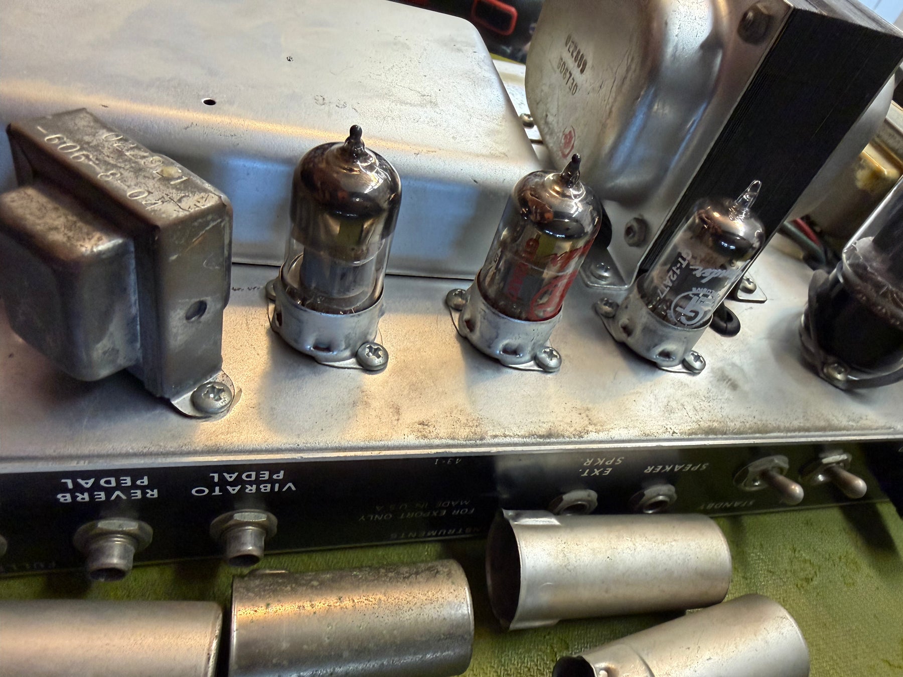 Close-up of the amp's silver chassis, showing three glowing vacuum tubes, two metal transformers, and several pedal inputs.
