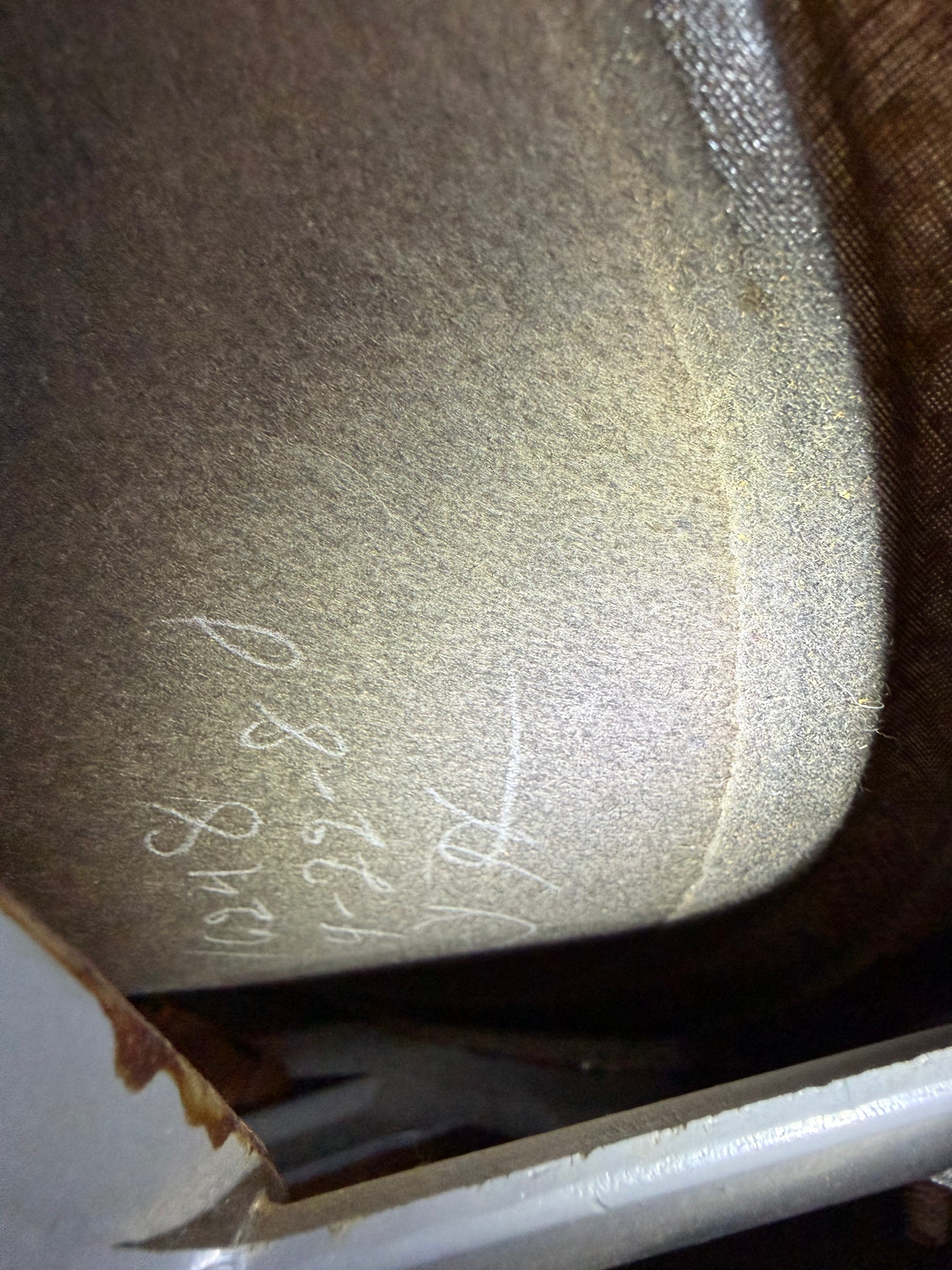 Close-up of a speaker cone's grey felt, with faint white handwritten numbers and a rusty metal edge visible below.