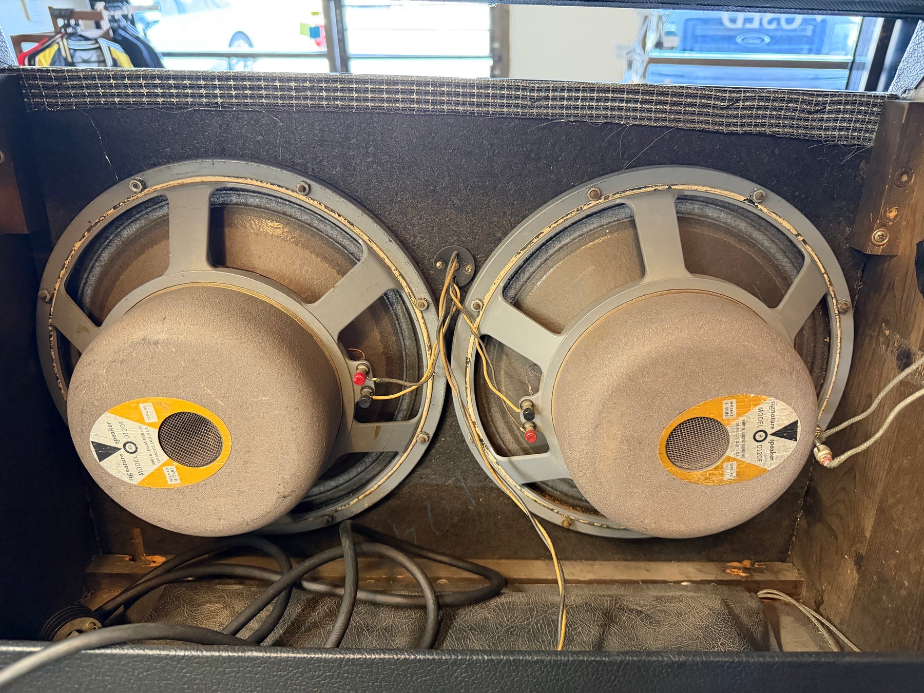 Rear view of the amp's two large, dusty speakers with visible wiring, mounted in a worn black cabinet with a checkered top edge.