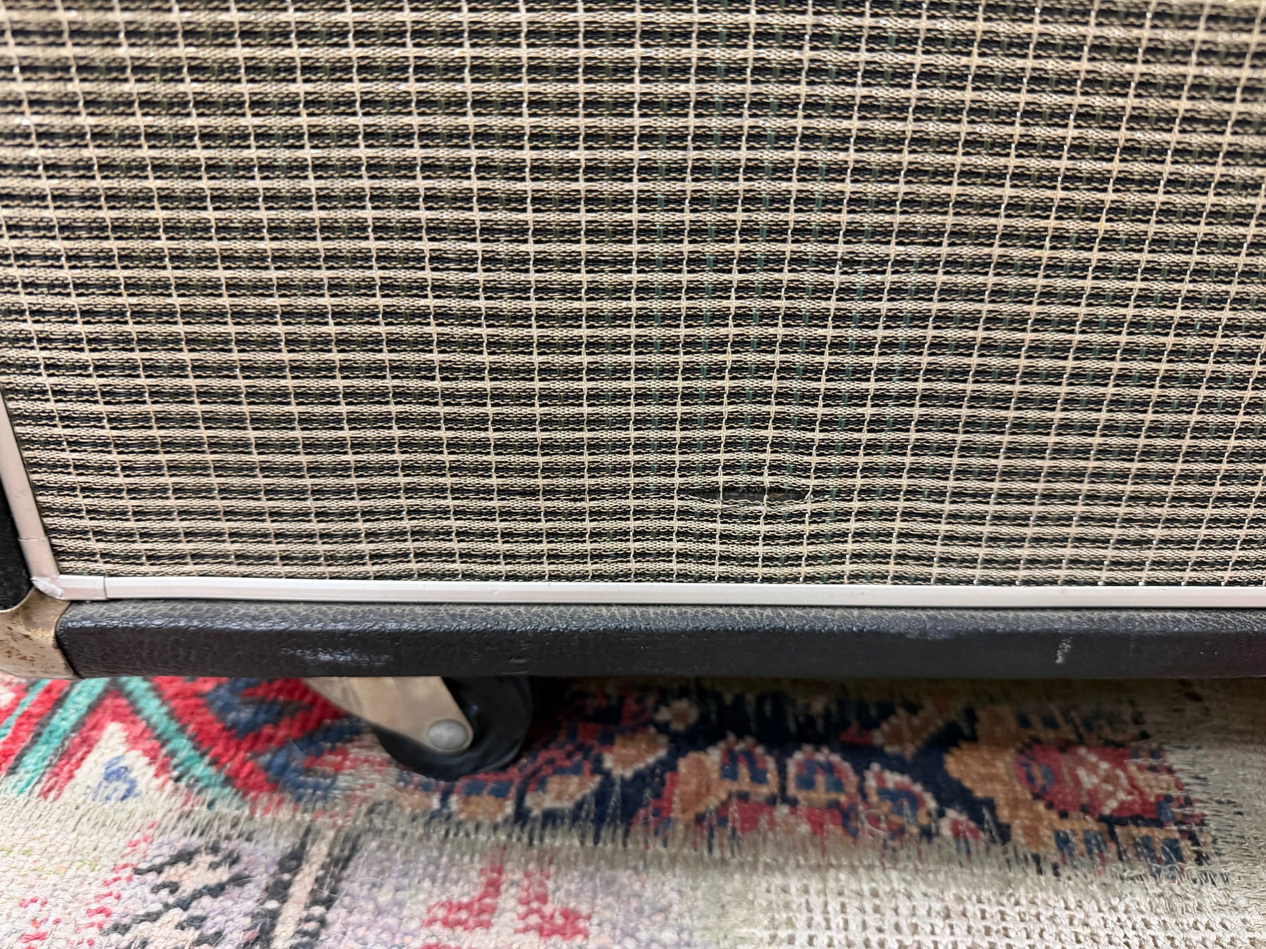 Close-up of the amp's lower right, showing the black grille cloth, white trim, black tolex, and a visible caster wheel.
