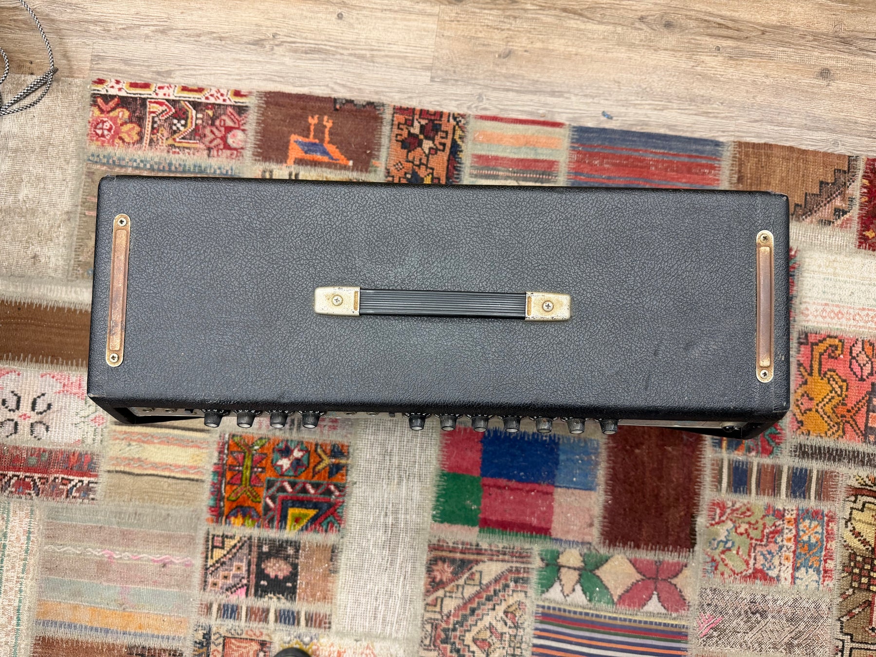 Overhead view of a black textured amp head with a black handle, brass hardware, and a row of silver knobs along the front.
