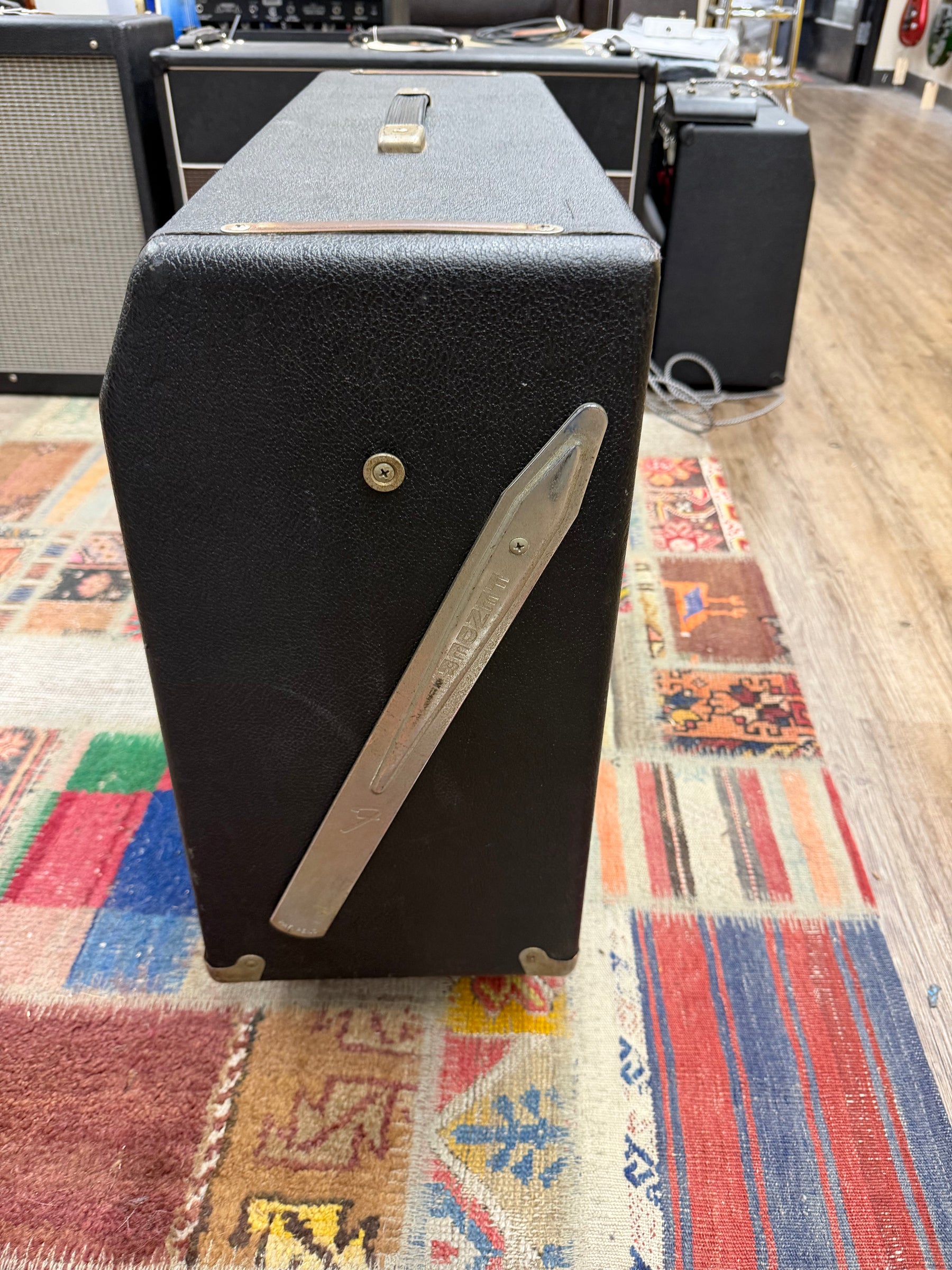 The black tolex amp is seen from the top-right, showing a metal tilt-back leg, a handle, and some scuffs on the finish.