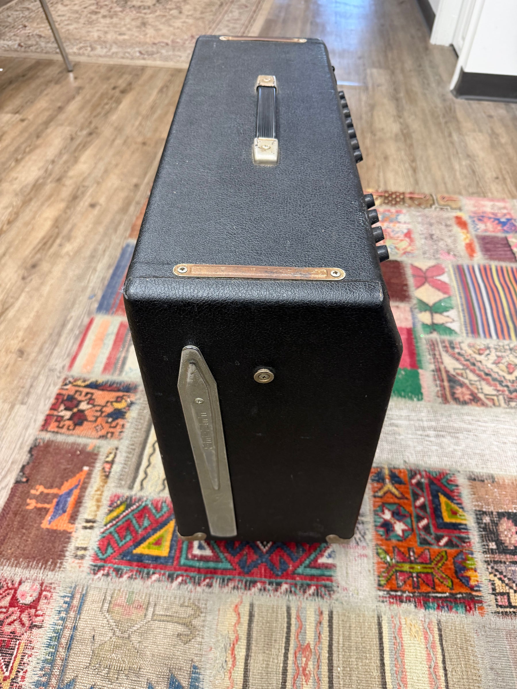 Top-down view of the black textured amp, showing its gold-plated handle, worn brown trim, and a silver tilt-back leg.