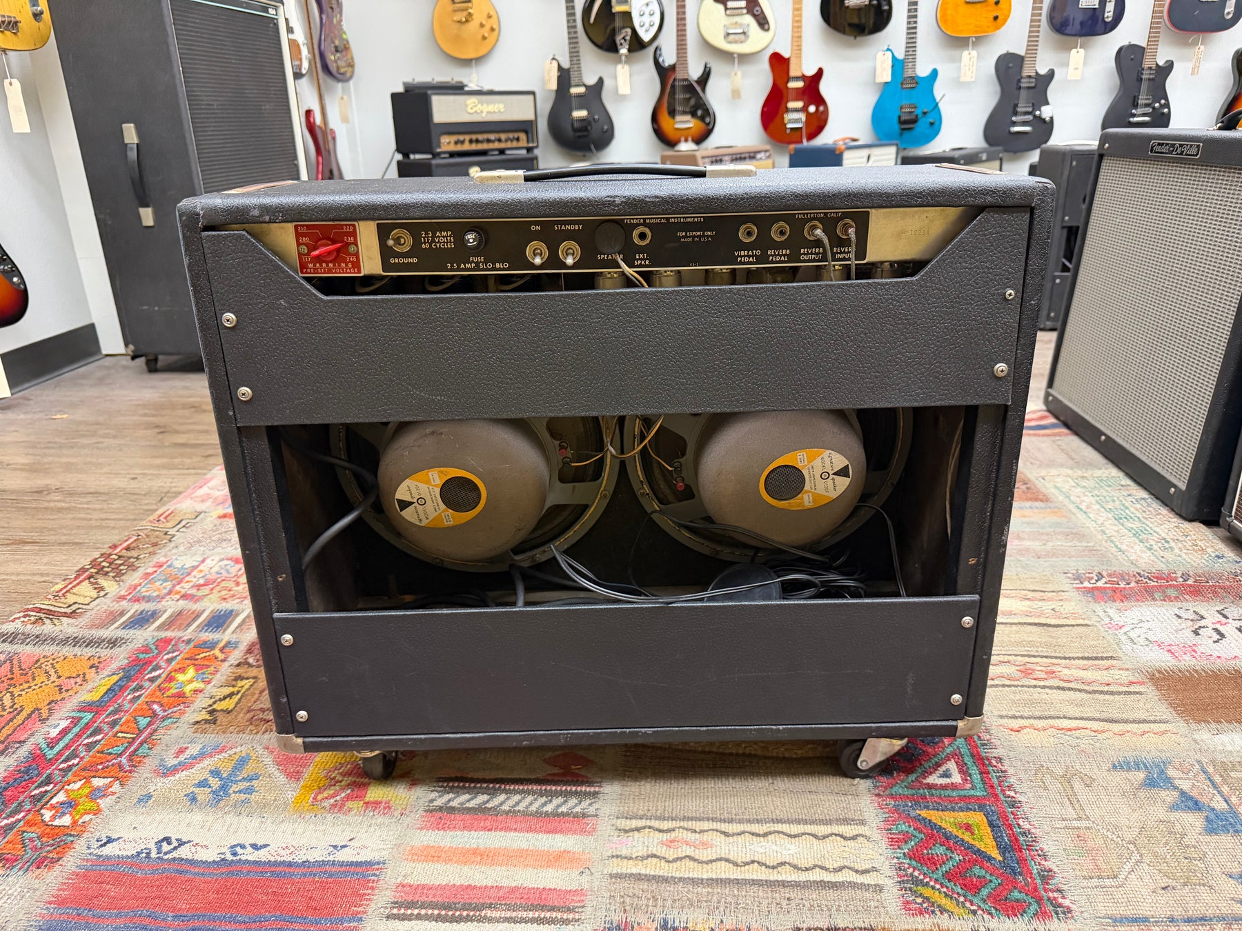 Rear view of a black tolex amp, showing the control panel, two visible JBL speakers, and casters on the bottom.