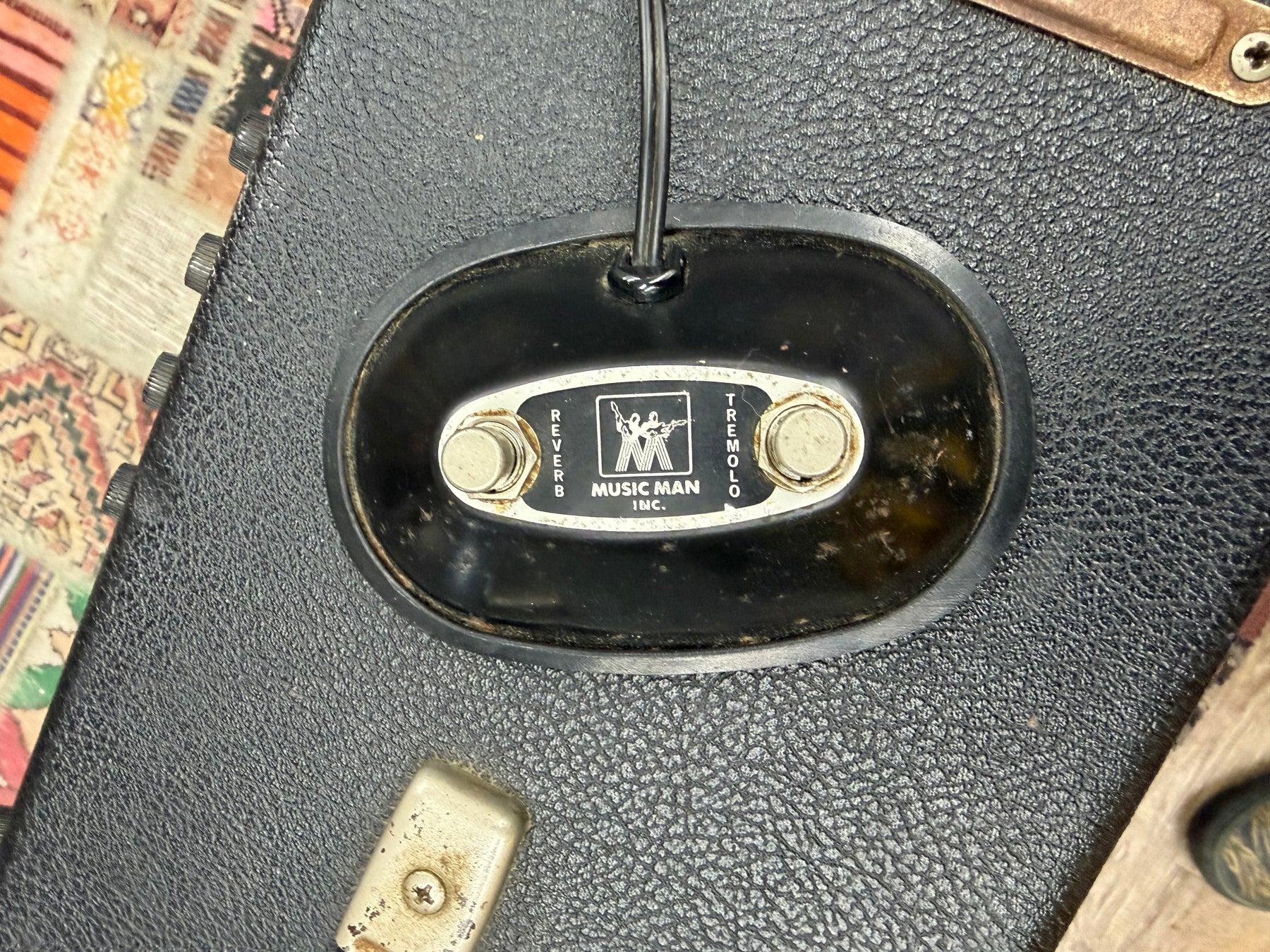 Close-up of a black, textured footswitch with two silver buttons labeled "Reverb" and "Tremolo," showing wear and rust.