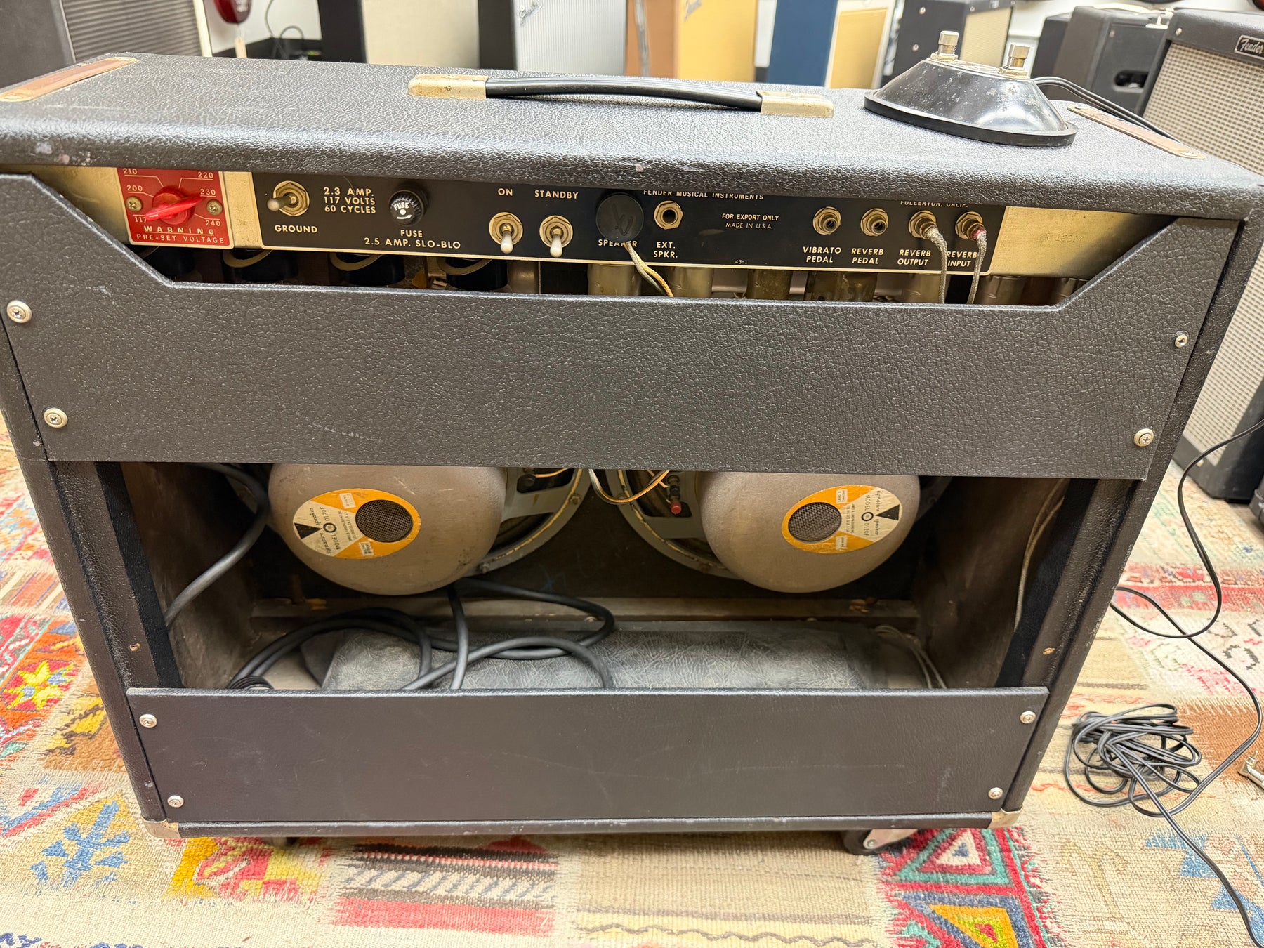 Rear view of a black textured amp with two visible speakers, a red voltage switch, and various inputs on the control panel.
