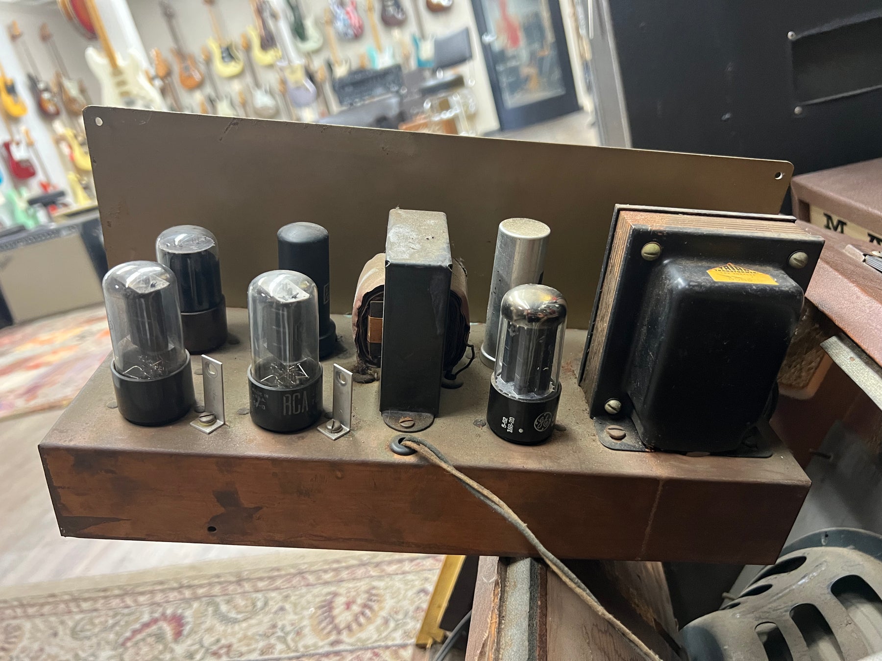 Overhead view of the amp's exposed chassis, showing eight vacuum tubes and two transformers on a tarnished copper-colored base.