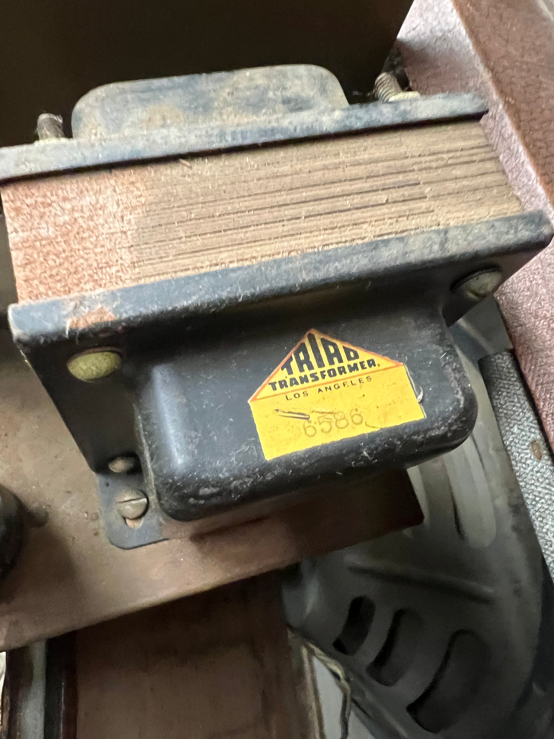 Close-up of a dusty, dark grey transformer with a yellow "TRIAD TRANSFORMER" label, showing rust and wear on the metal.
