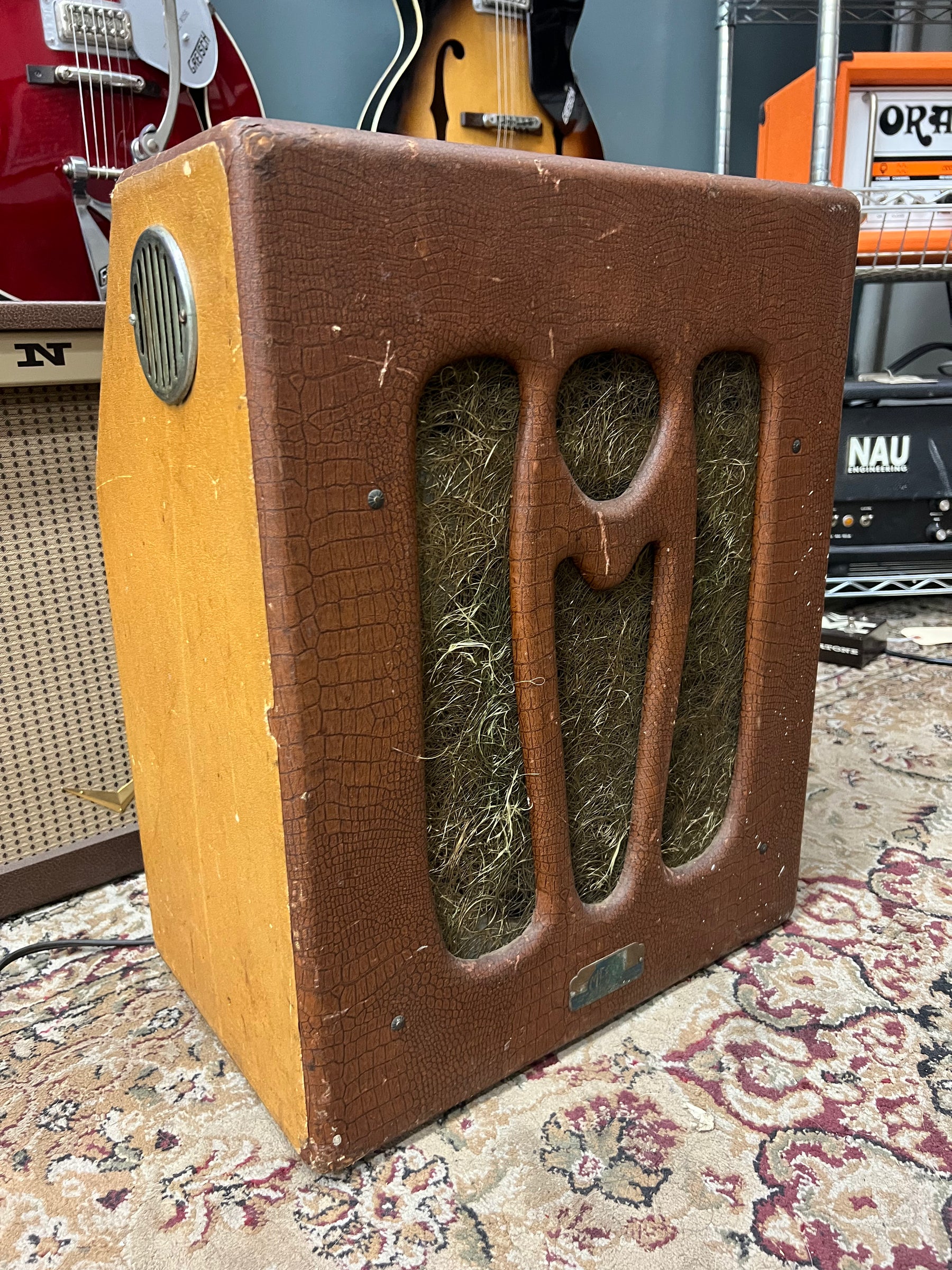 A vintage combo amp, angled to show its brown alligator-textured front with a cutout grill and a circular vent on the left side.