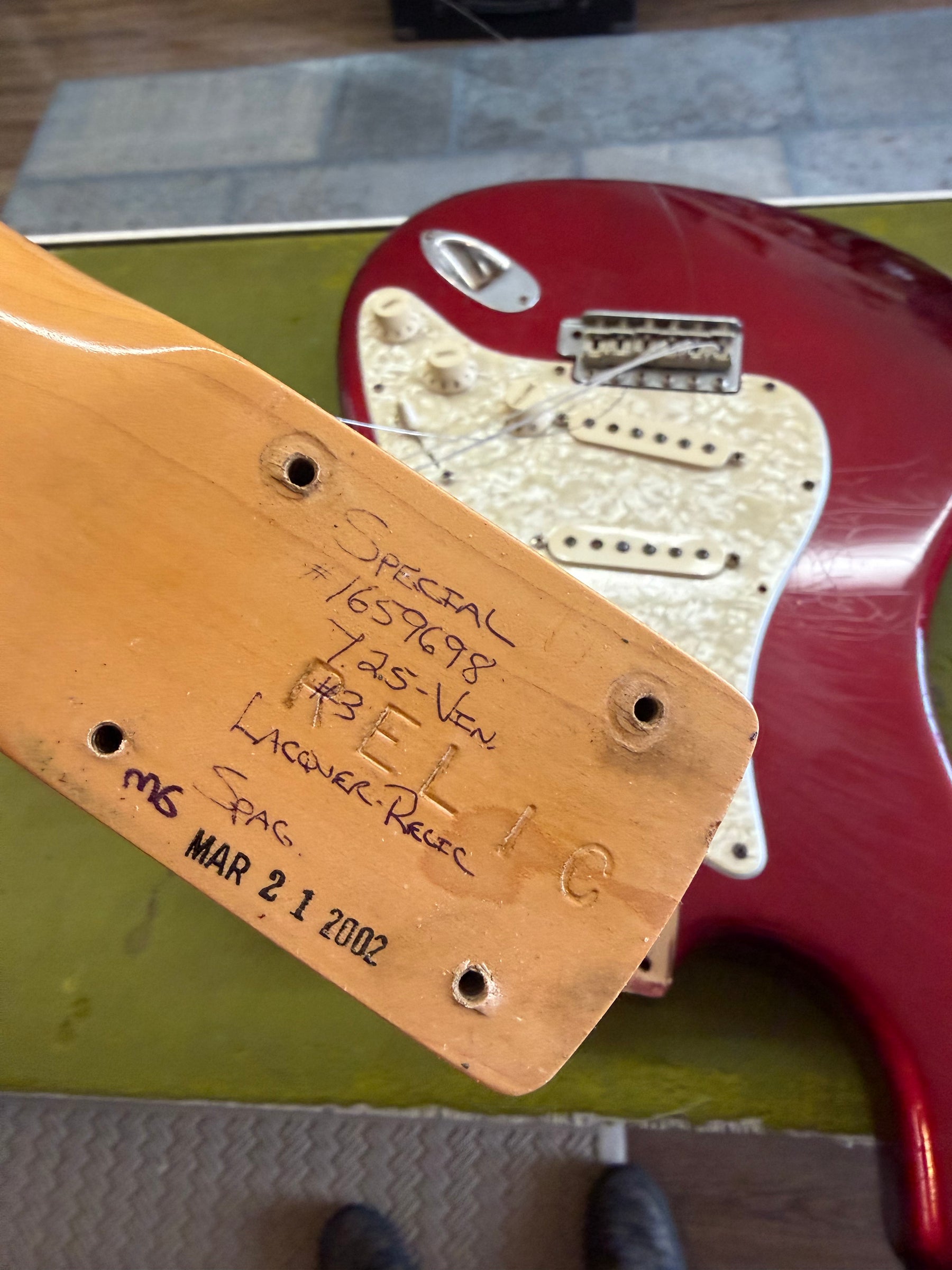 The guitar's neck heel, with handwritten "RELIC" and "MAR 21 2002" markings, is shown above the Candy Apple Red body.