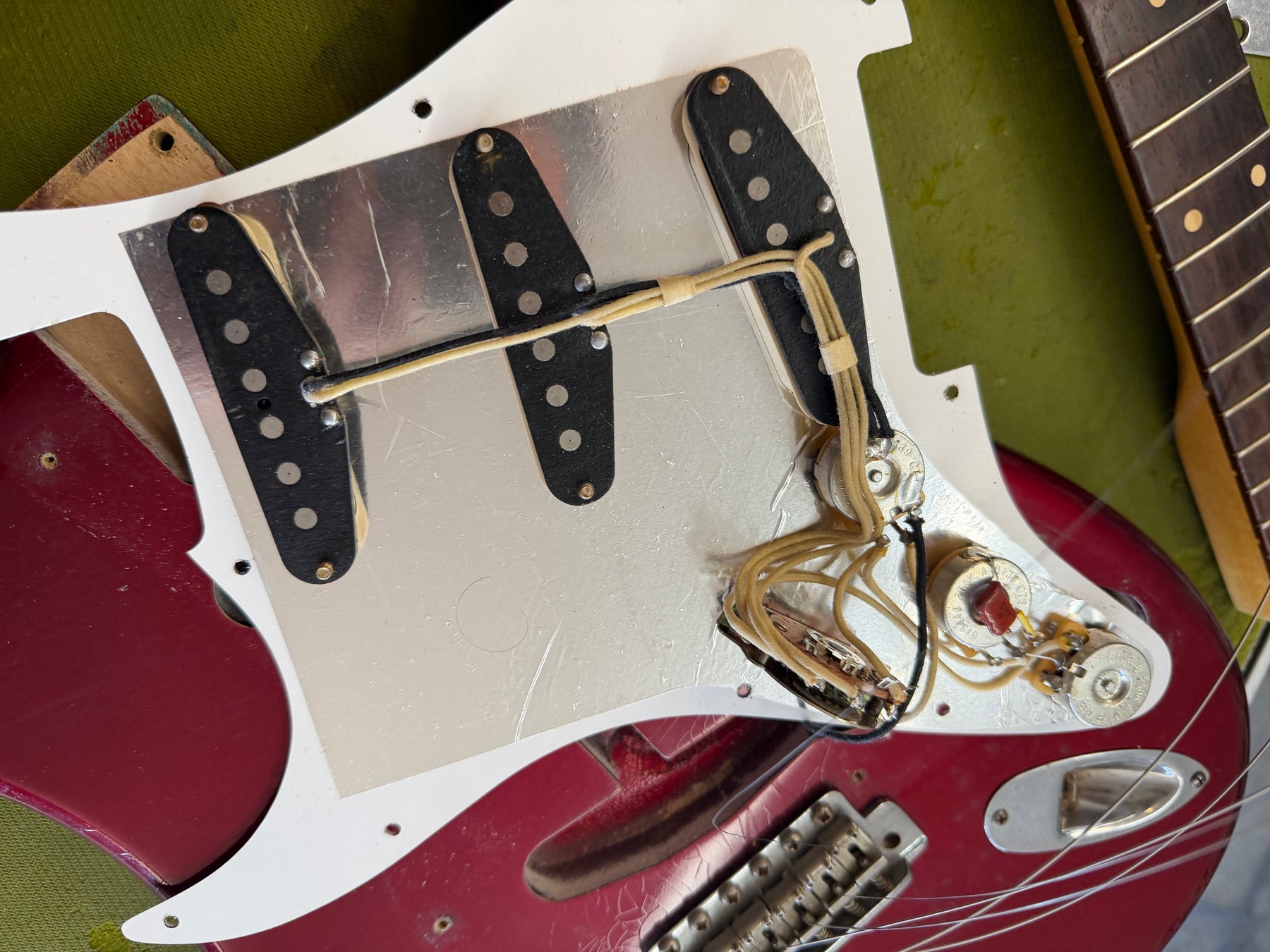 Close-up of the guitar's body, showing the back of the white pickguard removed, revealing three black pickups and wiring.