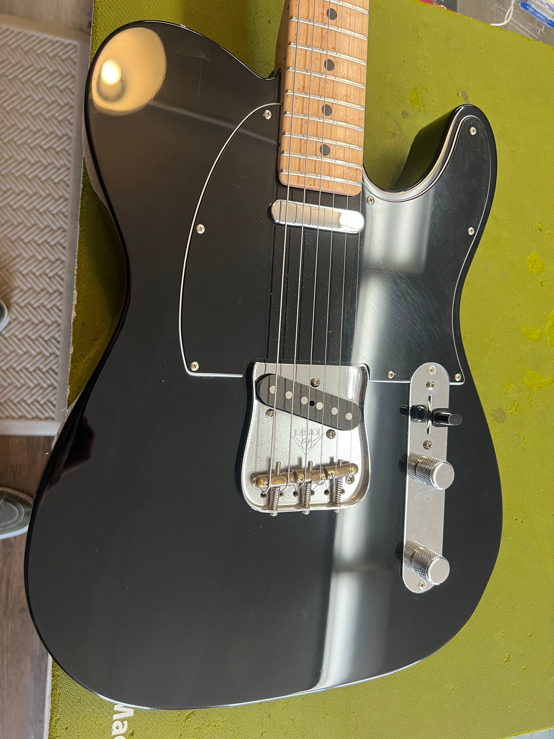 Black Telecaster body with a maple neck, chrome bridge and control plate, and a black pickguard, showing light surface scratches.