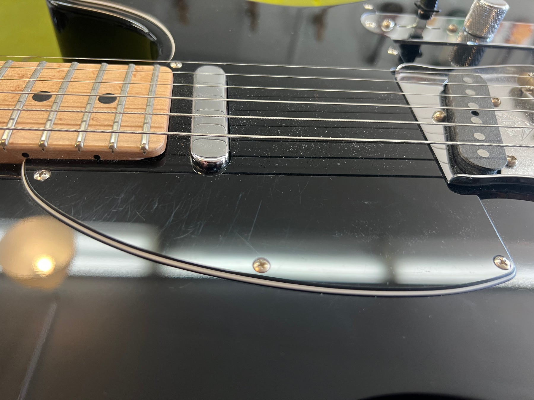 Close-up of the black guitar body and pickguard, showing light scratches, with the neck pickup and lower fretboard visible.