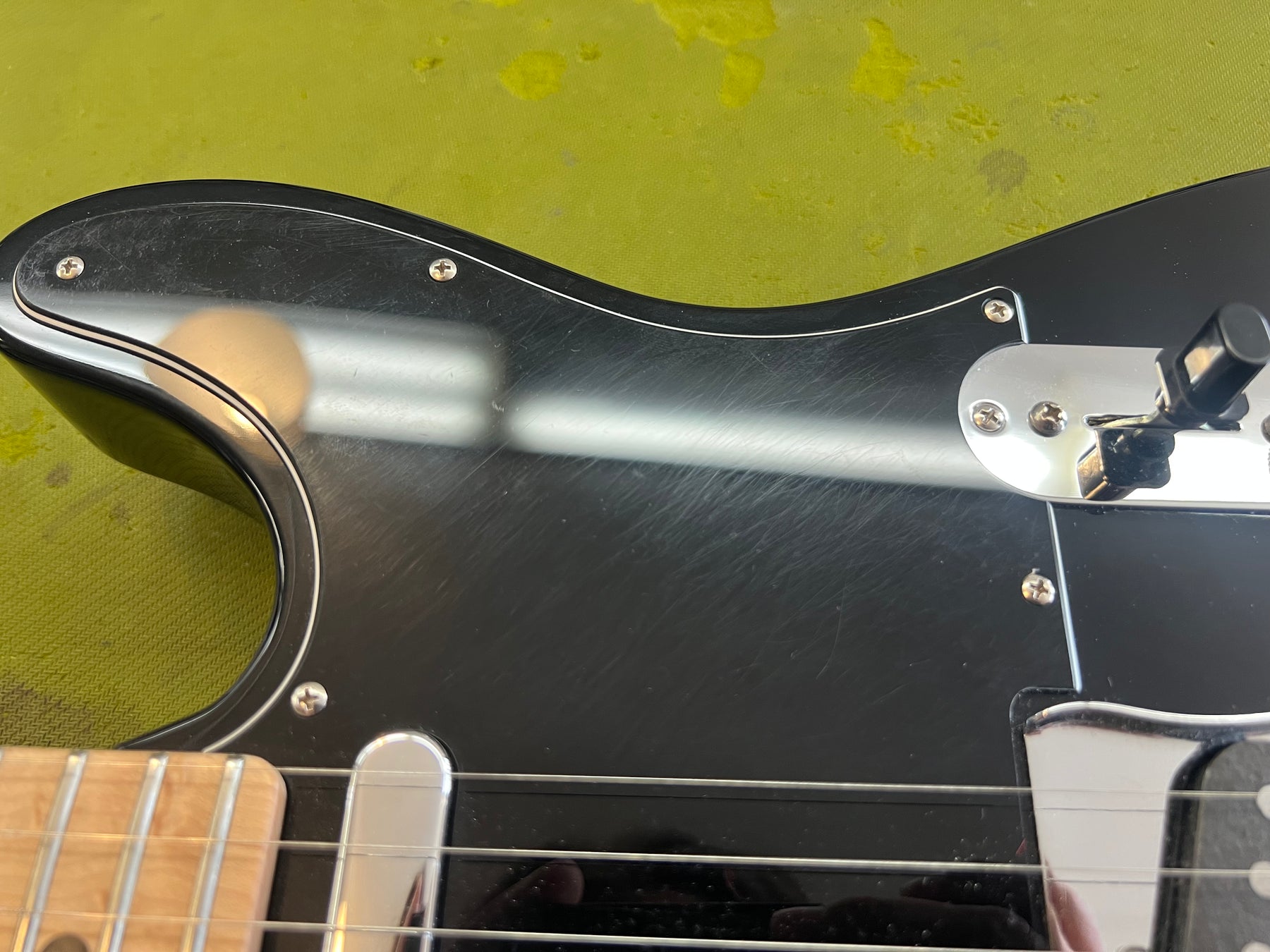 Close-up of the black pickguard and control plate, showing many light scratches and a black switch tip.