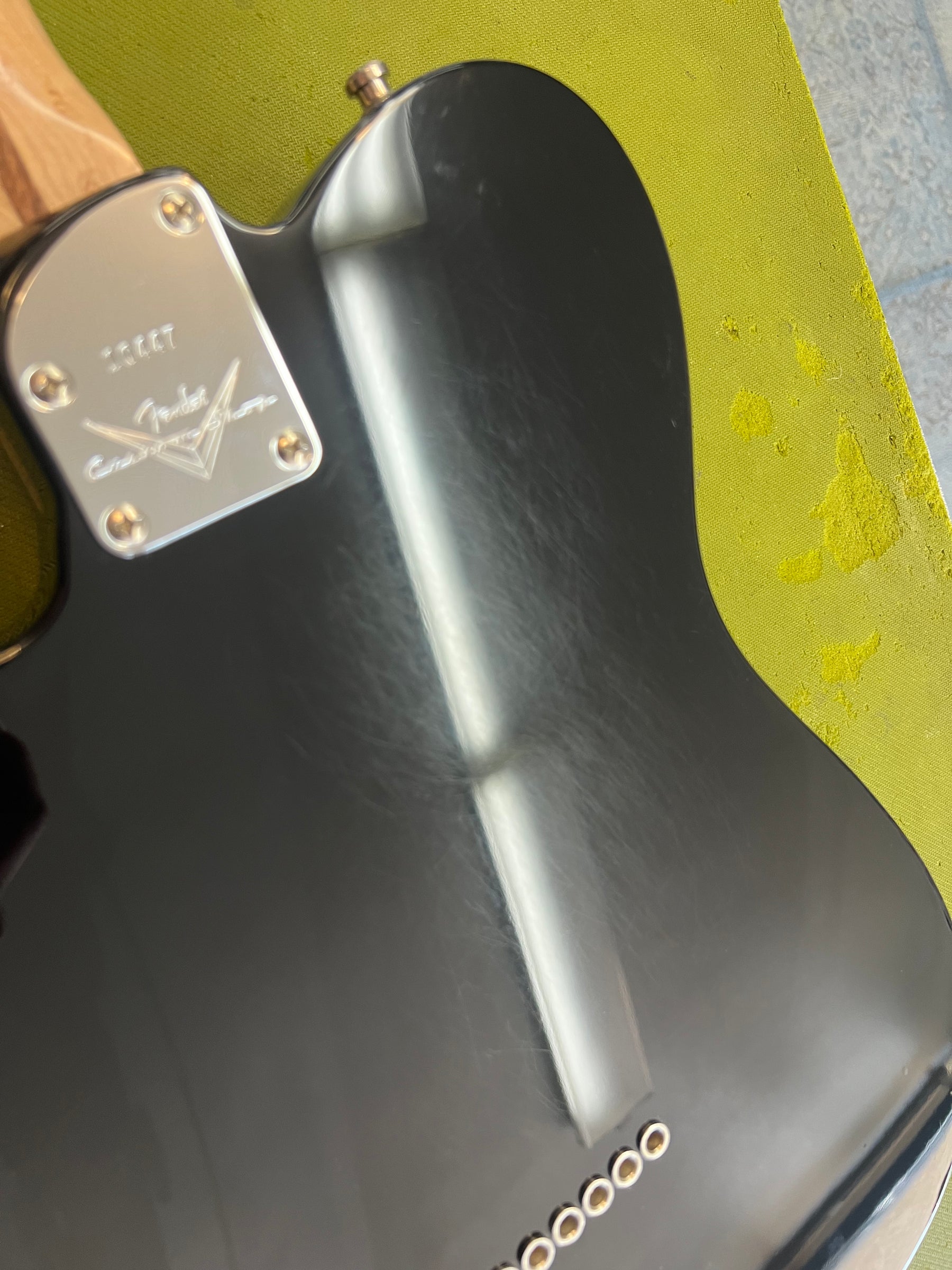 The black Telecaster's back shows light surface scratches, a chrome neck plate, and six gold string-through-body ferrules.